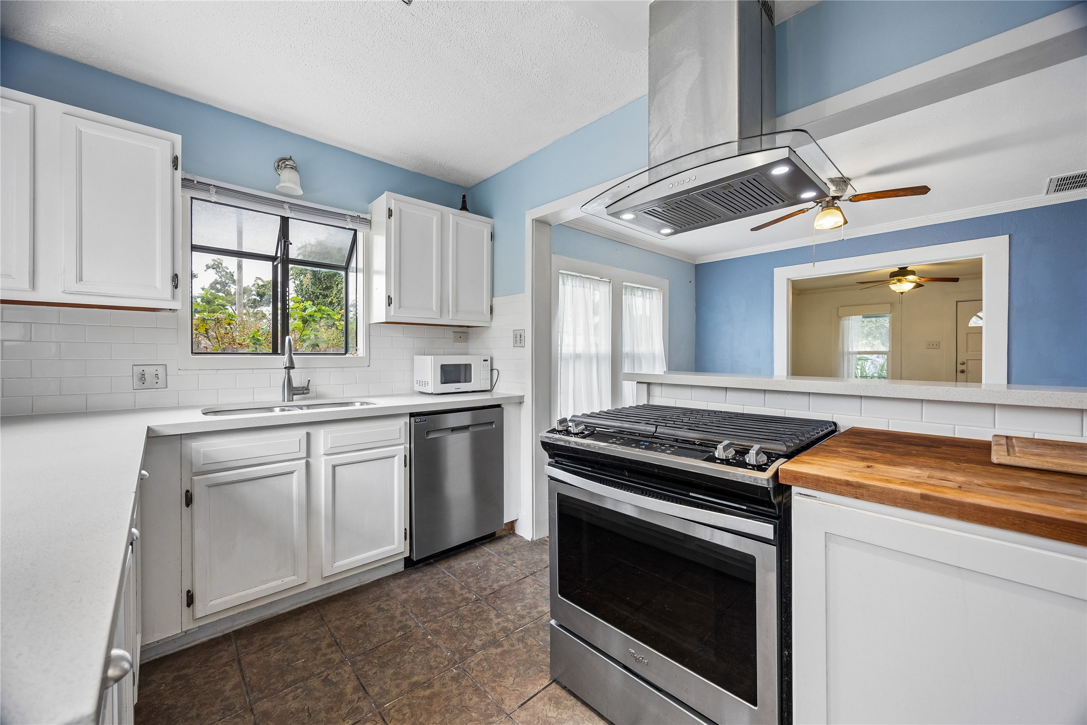 Another view of the kitchen showcases its cheerful blue-and-white palette, stainless-steel appliances, butcher-block counter accent, and convenient opening to the adjoining room.