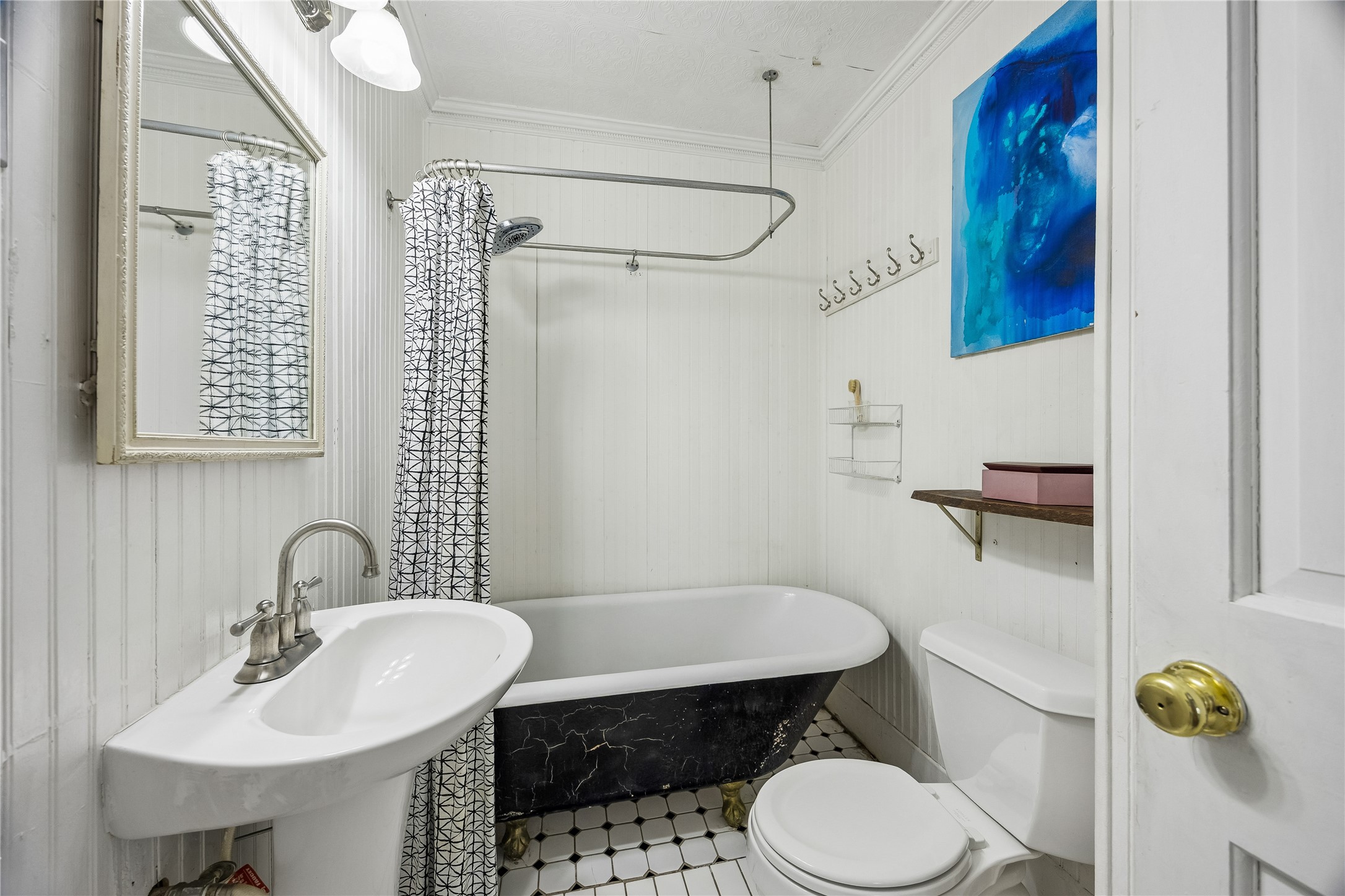 Vintage character shines in this bath, where a classic clawfoot-style tub, pedestal sink, paneled walls, and patterned tile floor create a delightfully distinctive space.