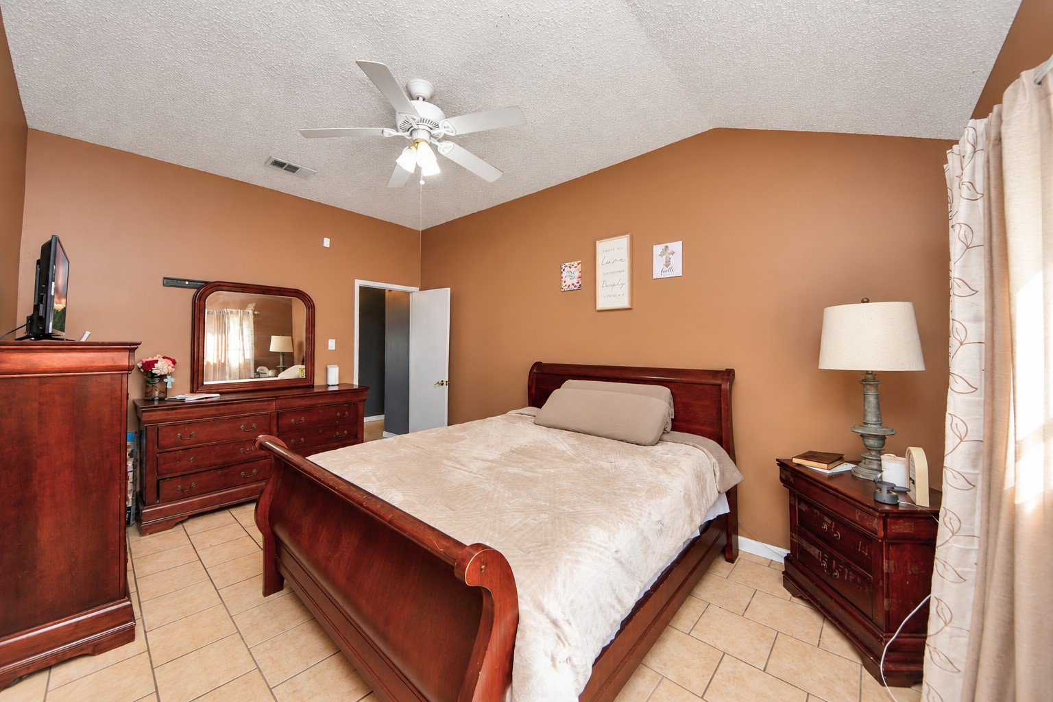 Spacious primary bedroom featuring tile flooring, a vaulted ceiling, and a ceiling fan for added comfort. Generous wall space and natural light create a welcoming retreat with plenty of room for your bedroom furnishings.
