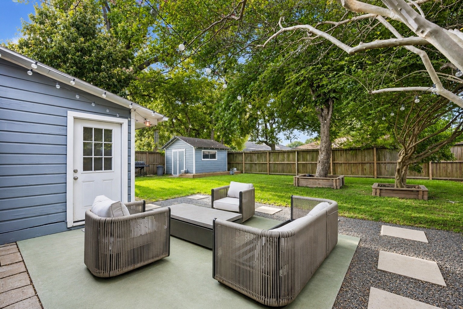 Step outside to a patio designed for year round enjoyment, overlooking a beautifully maintained backyard shaded by mature trees. String lights, expansive green space, and a detached storage building create the perfect backdrop for outdoor entertaining, gardening, or weekend play.