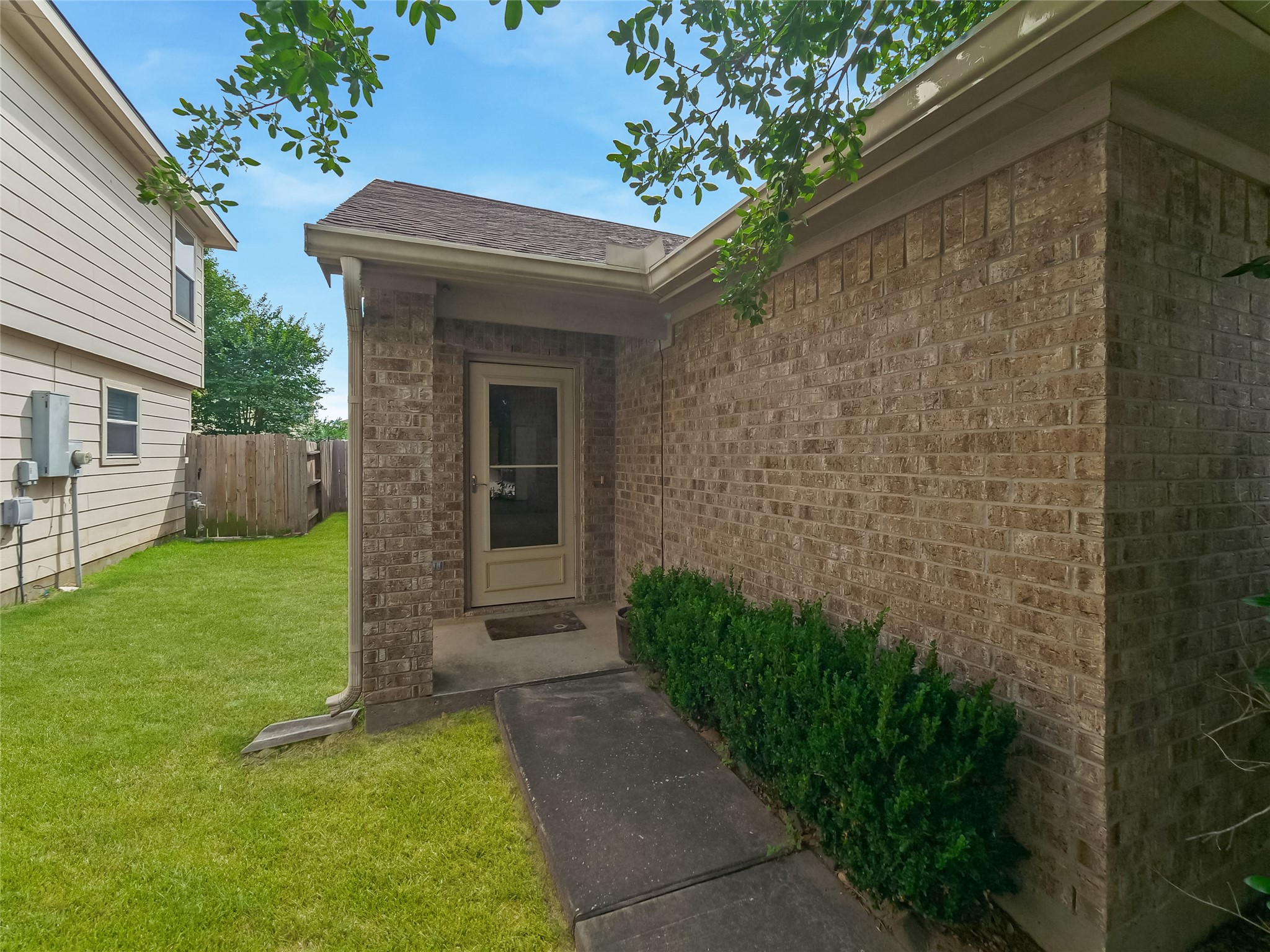Side entrance of the home with a brick exterior, front door, and neatly trimmed shrubs.