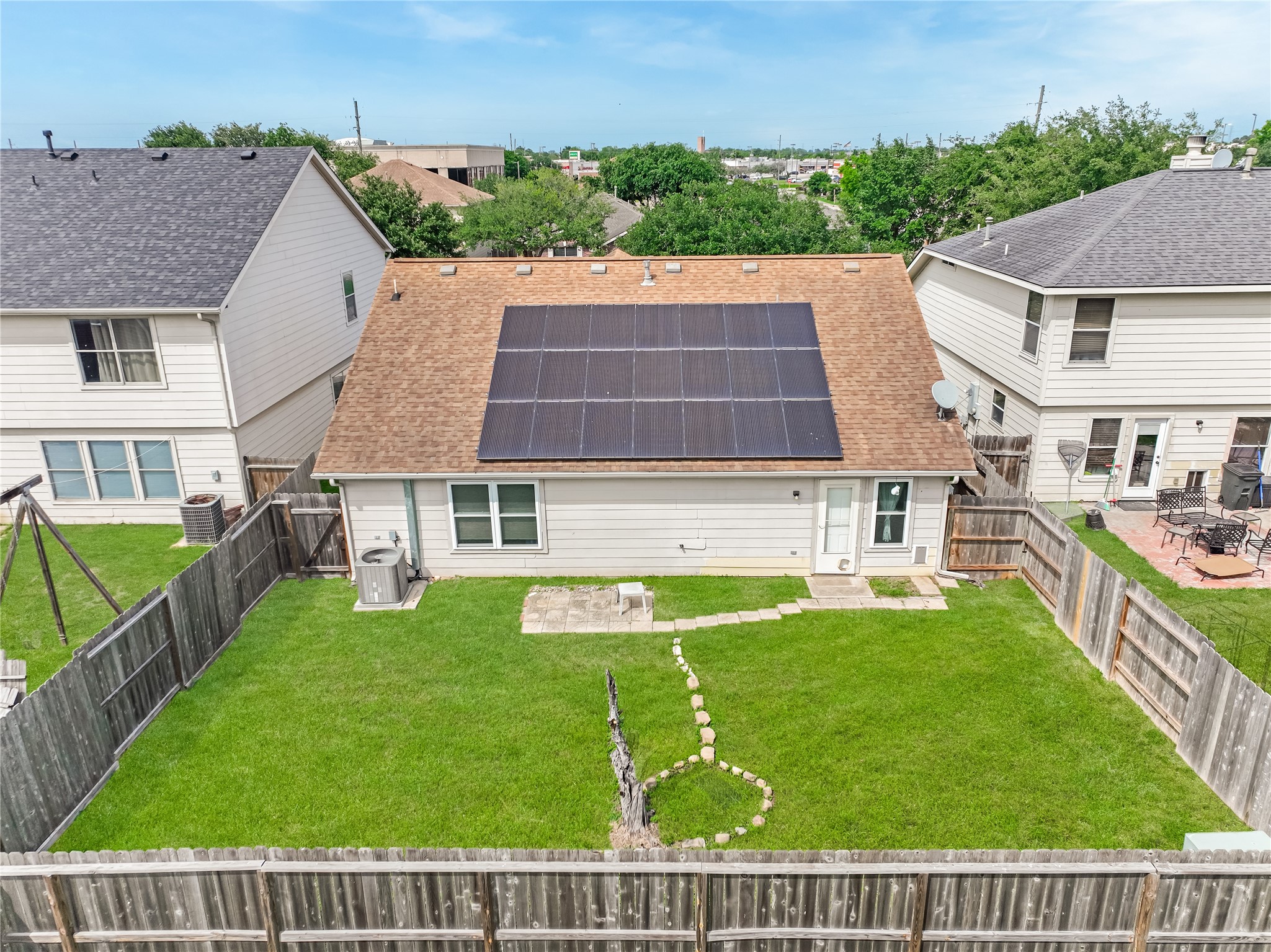 Rear exterior view of the house featuring a spacious backyard, landscaped lawn, & solar panels.