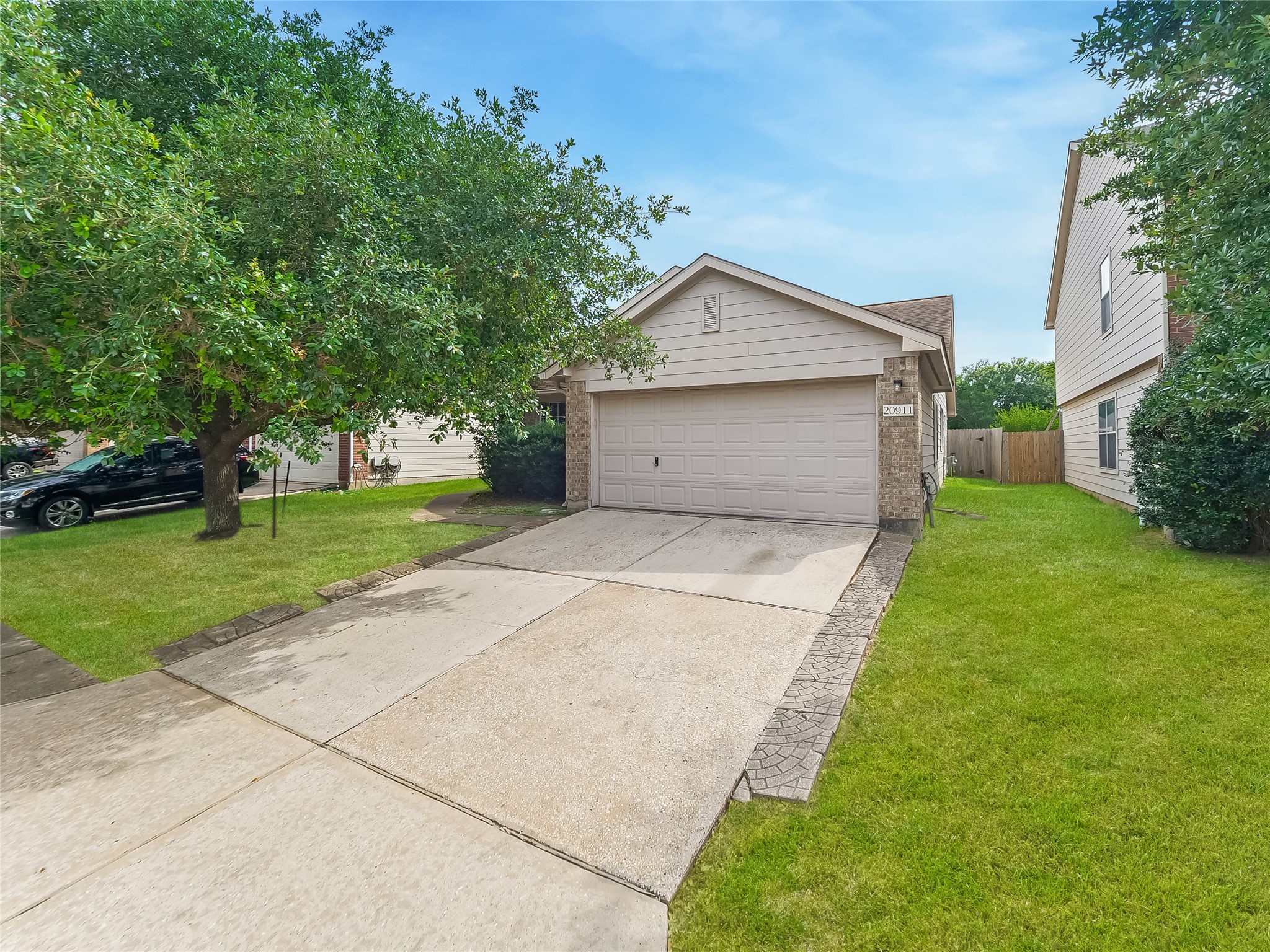 Wide view of the house and driveway, showing the attached garage, front lawn, and surrounding trees.