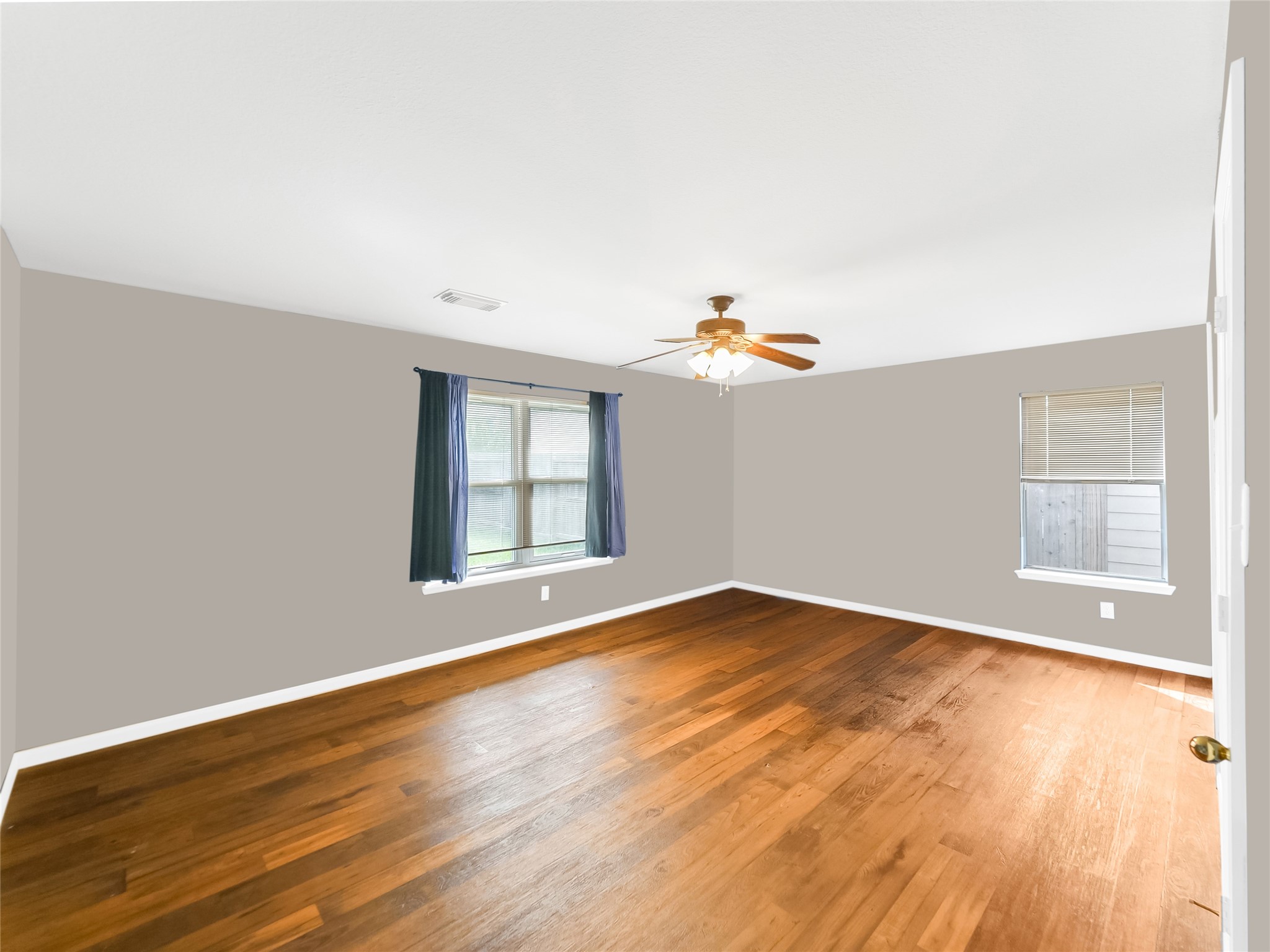 Spacious primary bedroom with wood flooring, windows, and a ceiling fan.