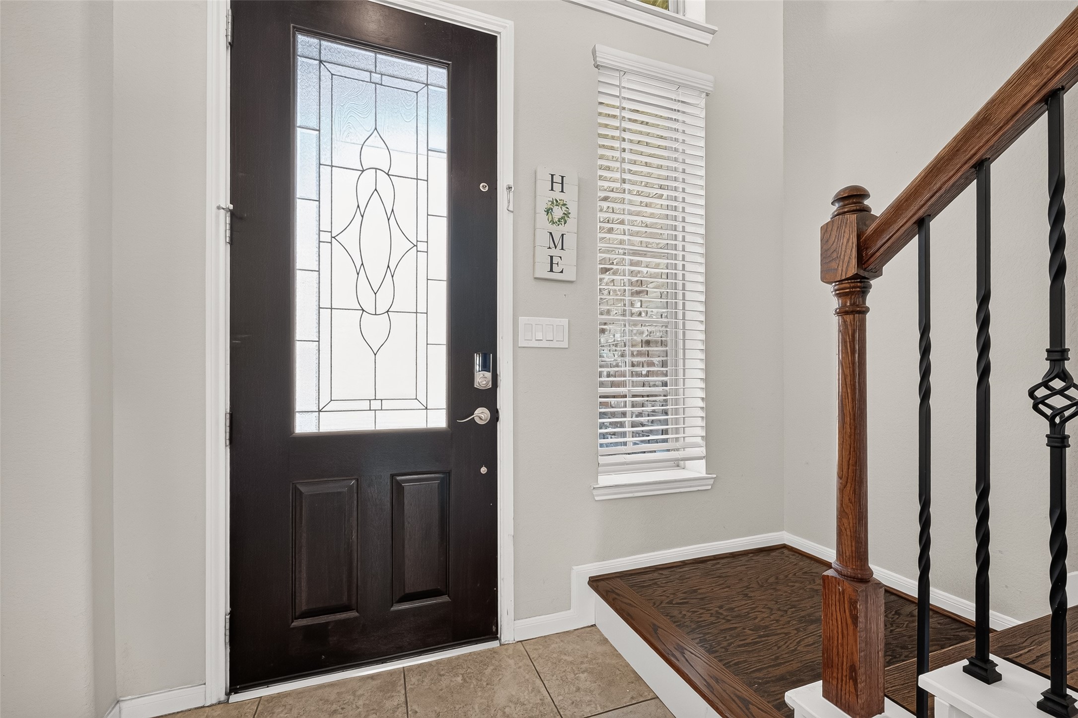 Natural light brightens the entry, with tile flooring and a wood staircase just inside.