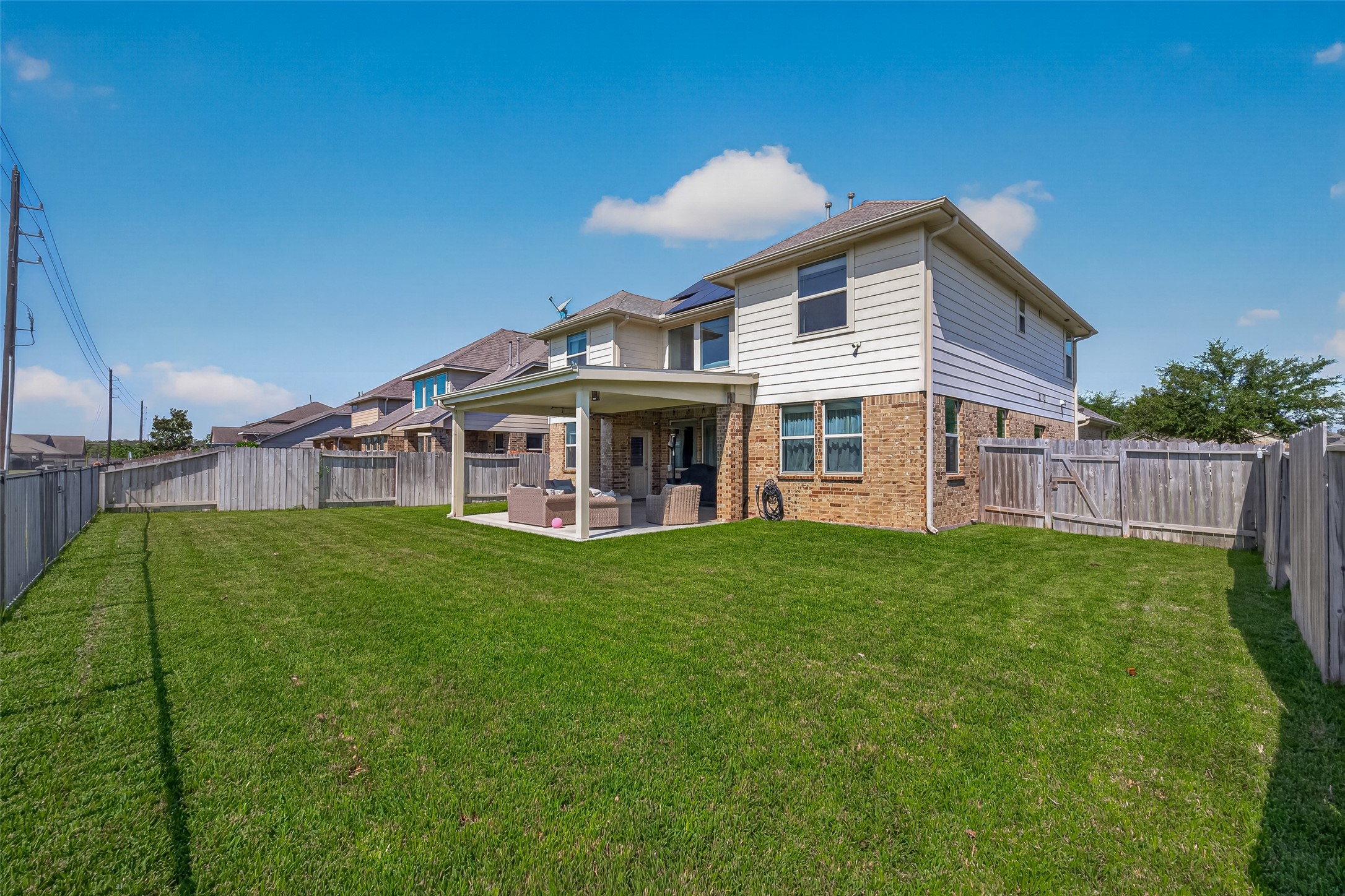 The rear exterior showcases the two-story layout, covered patio, and backyard lawn.