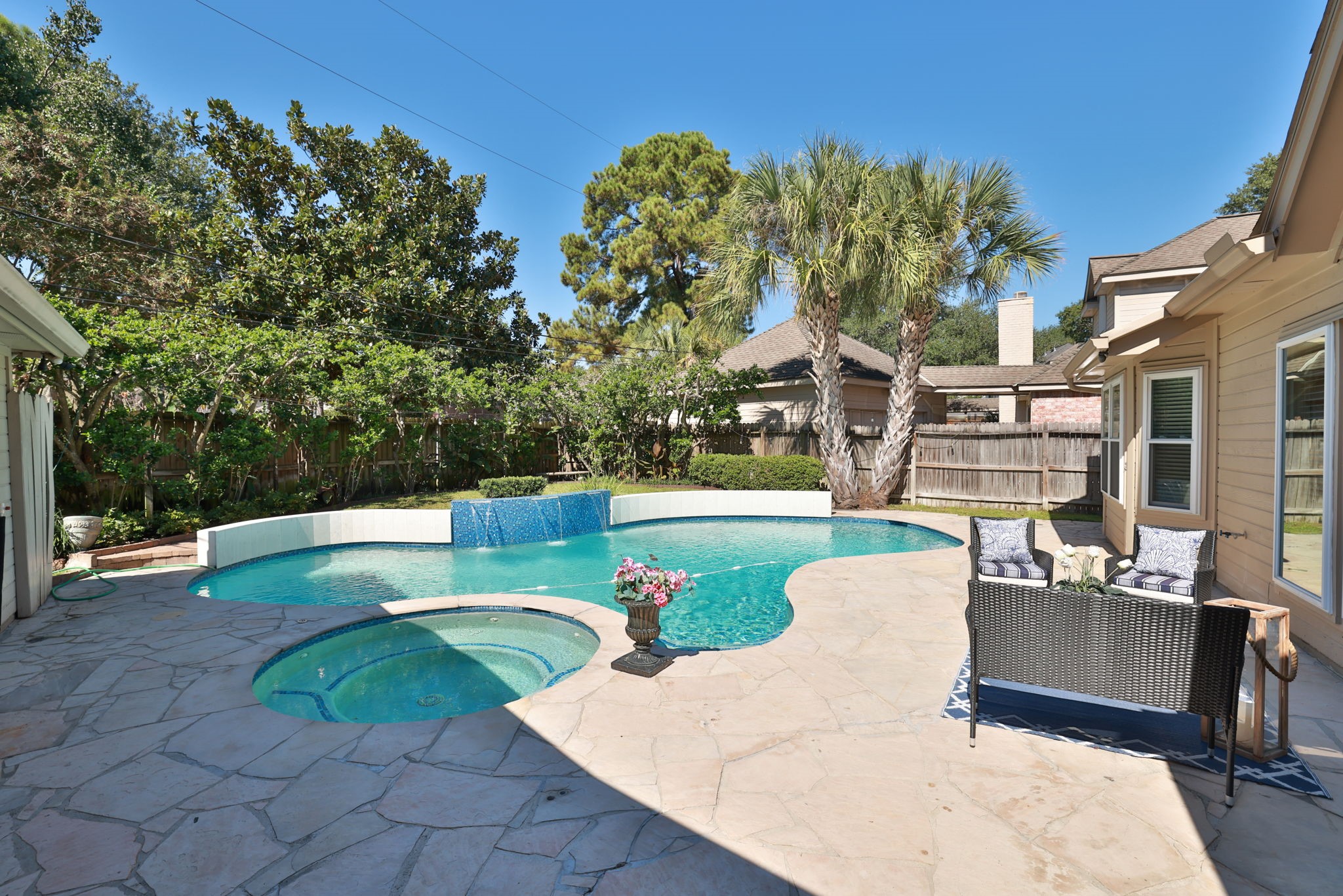 Private backyard oasis with sparkling pool, spa, and flagstone patio surrounded by lush landscaping.