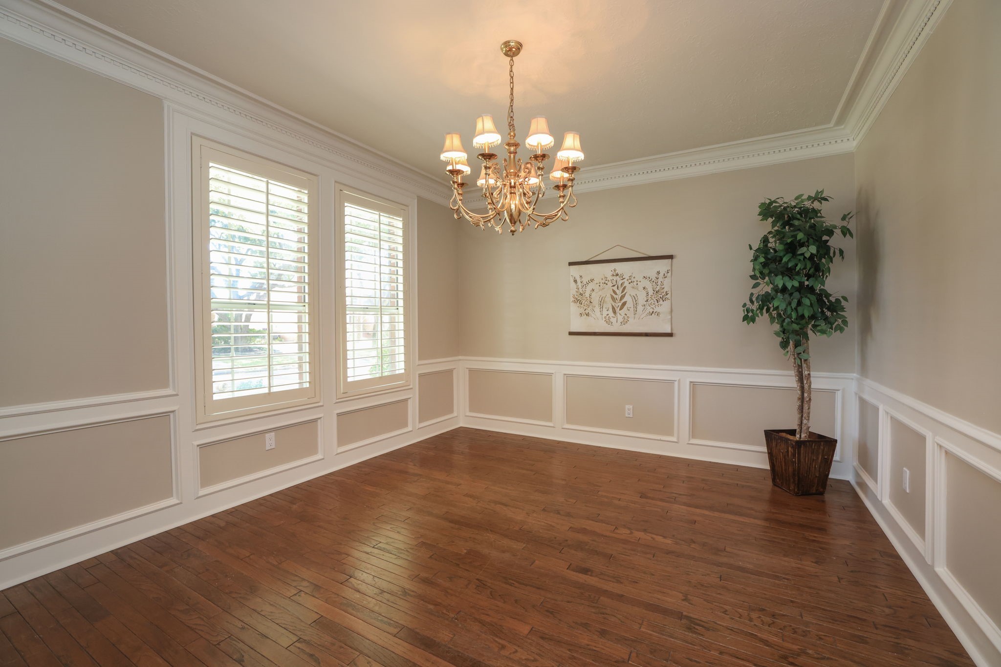 Elegant formal dining room with wood floors, designer chandelier, plantation shutters, and detailed wainscoting.