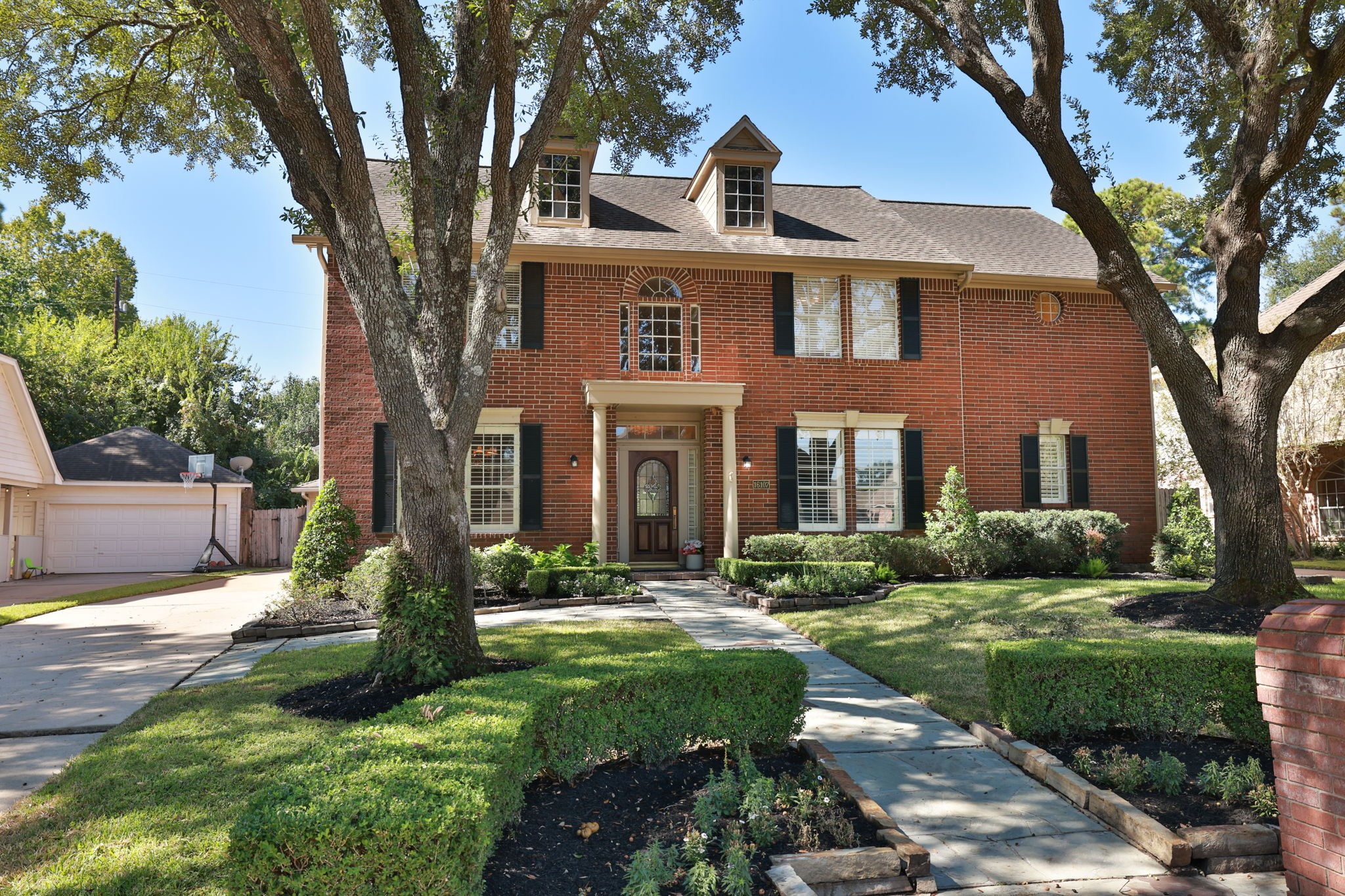 Perfectly balanced architecture with columned entry, black shutters, and freshly edged landscaping.