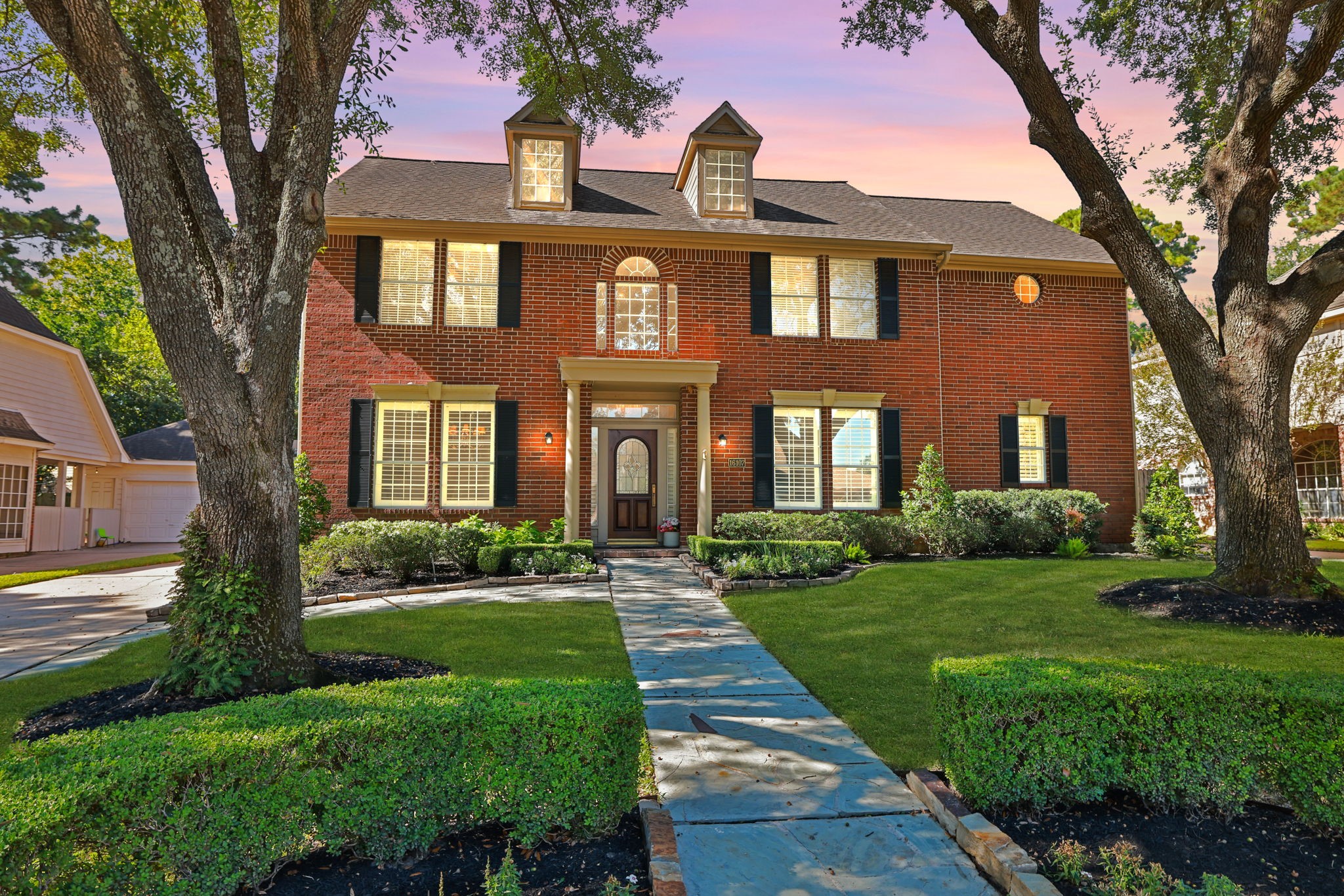 Classic Red Brick facade framed by mature trees and manicured landscaping offers timeless curb appeal.