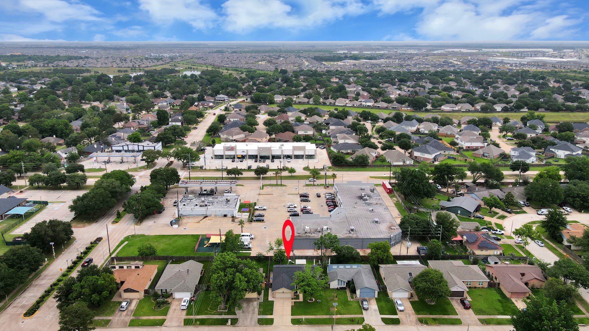This aerial photo showcases a suburban neighborhood with neatly arranged houses and lush greenery. A commercial area with shops is nearby, providing convenient access to amenities. The community is spacious, offering a peaceful residential environment.