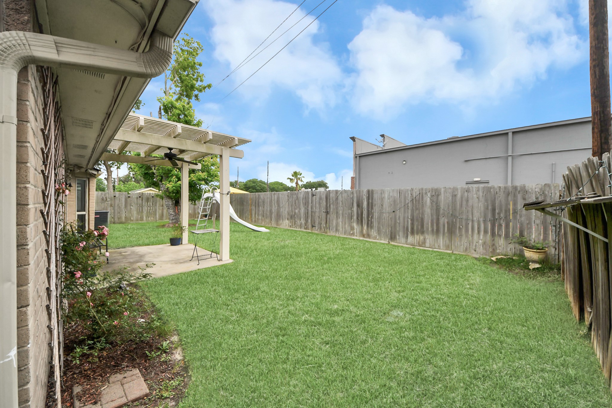 Spacious backyard featuring a grassy lawn, a patio with a pergola, and a slide for kids. The area is fenced for privacy, perfect for outdoor activities and relaxation.