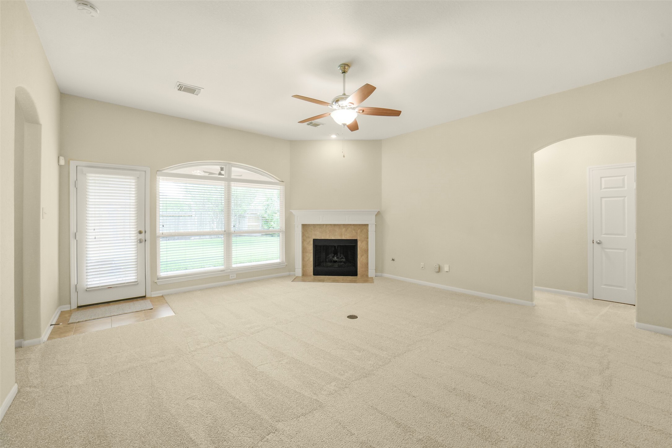 Spacious living room featuring a cozy fireplace, abundant natural light from large windows, and convenient backyard access through a glass door.