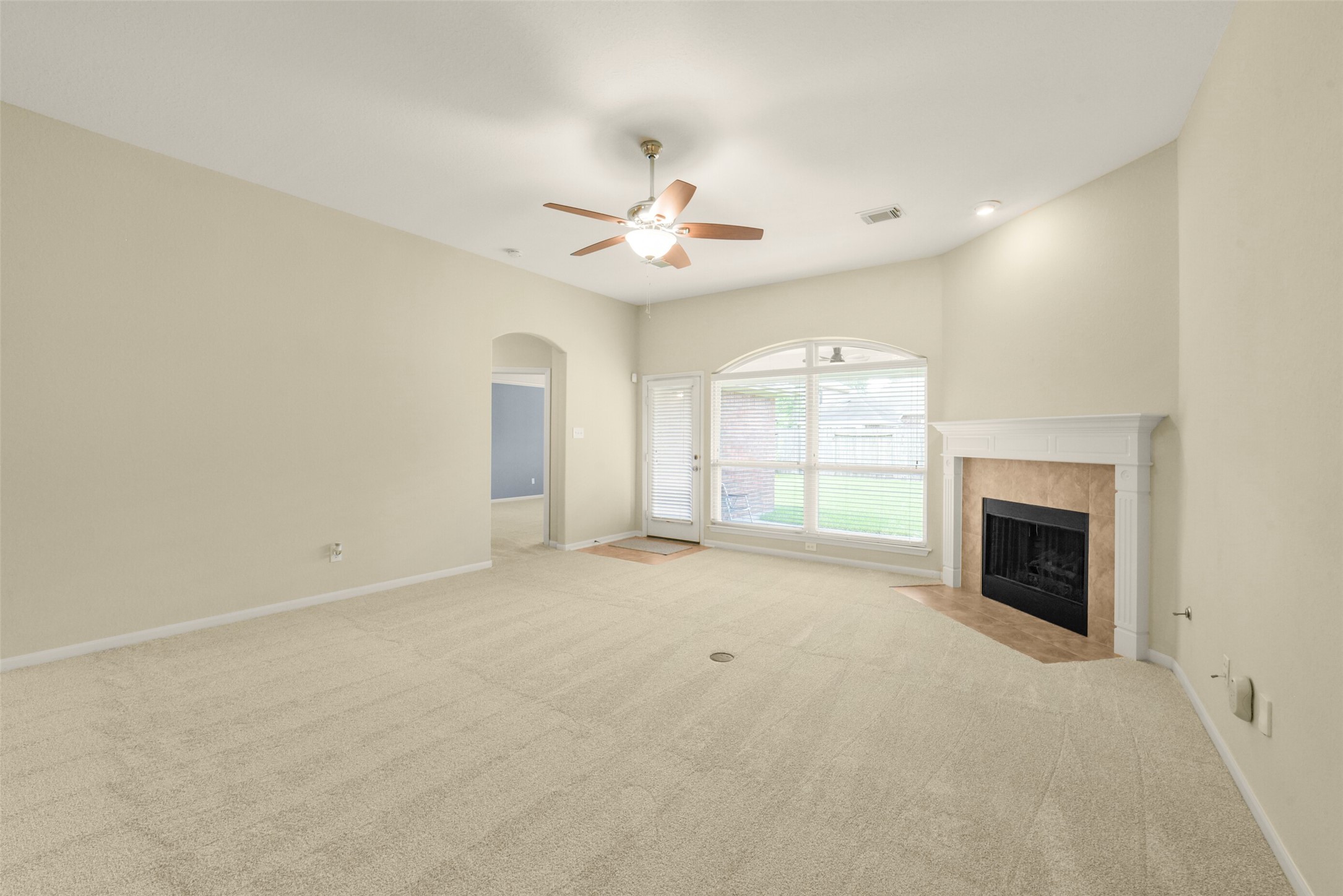 Spacious living room featuring a cozy fireplace, large window for natural light, and a ceiling fan for comfort.