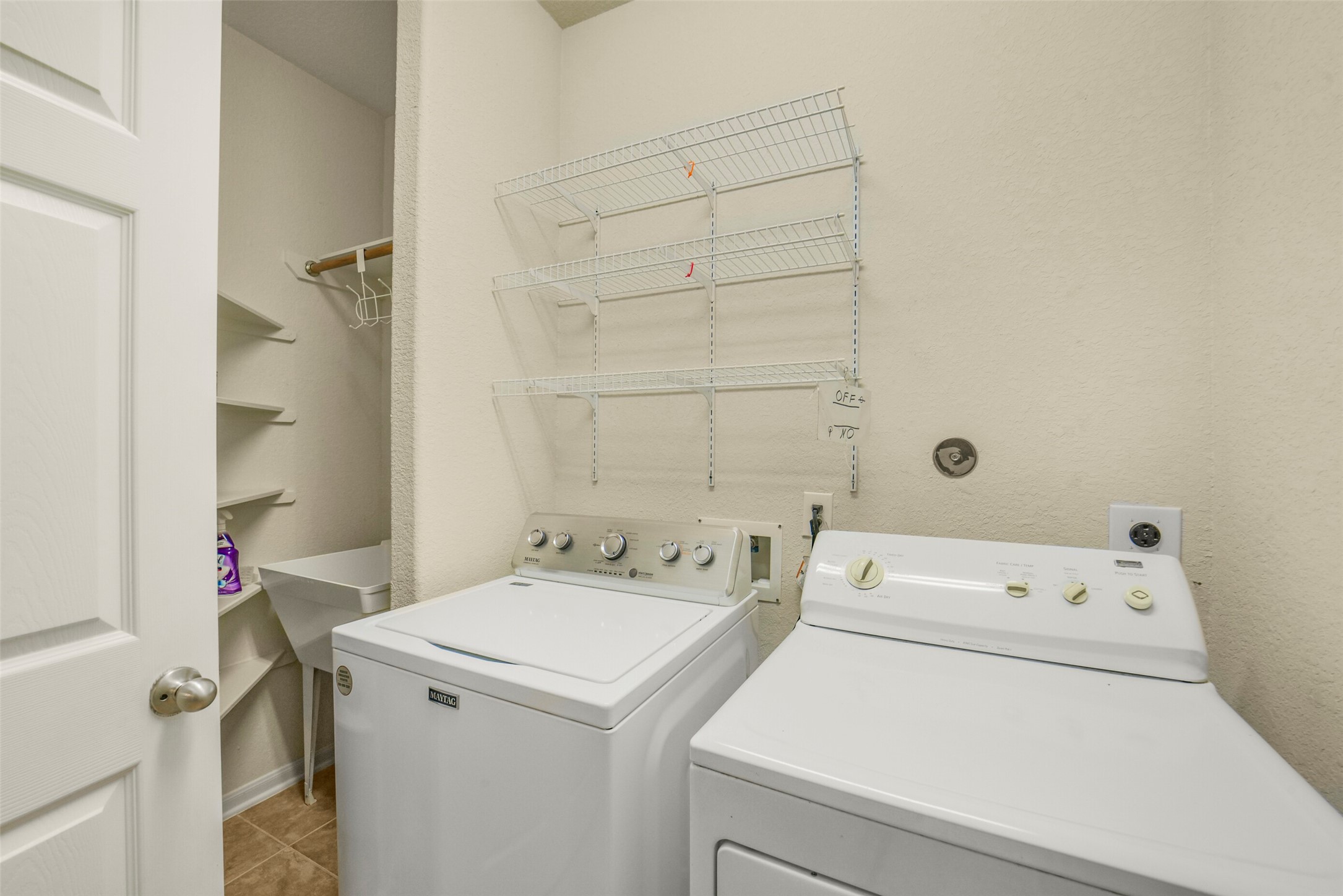 Large laundry room with washer and dryer, ample shelving, and a utility sink for added functionality.