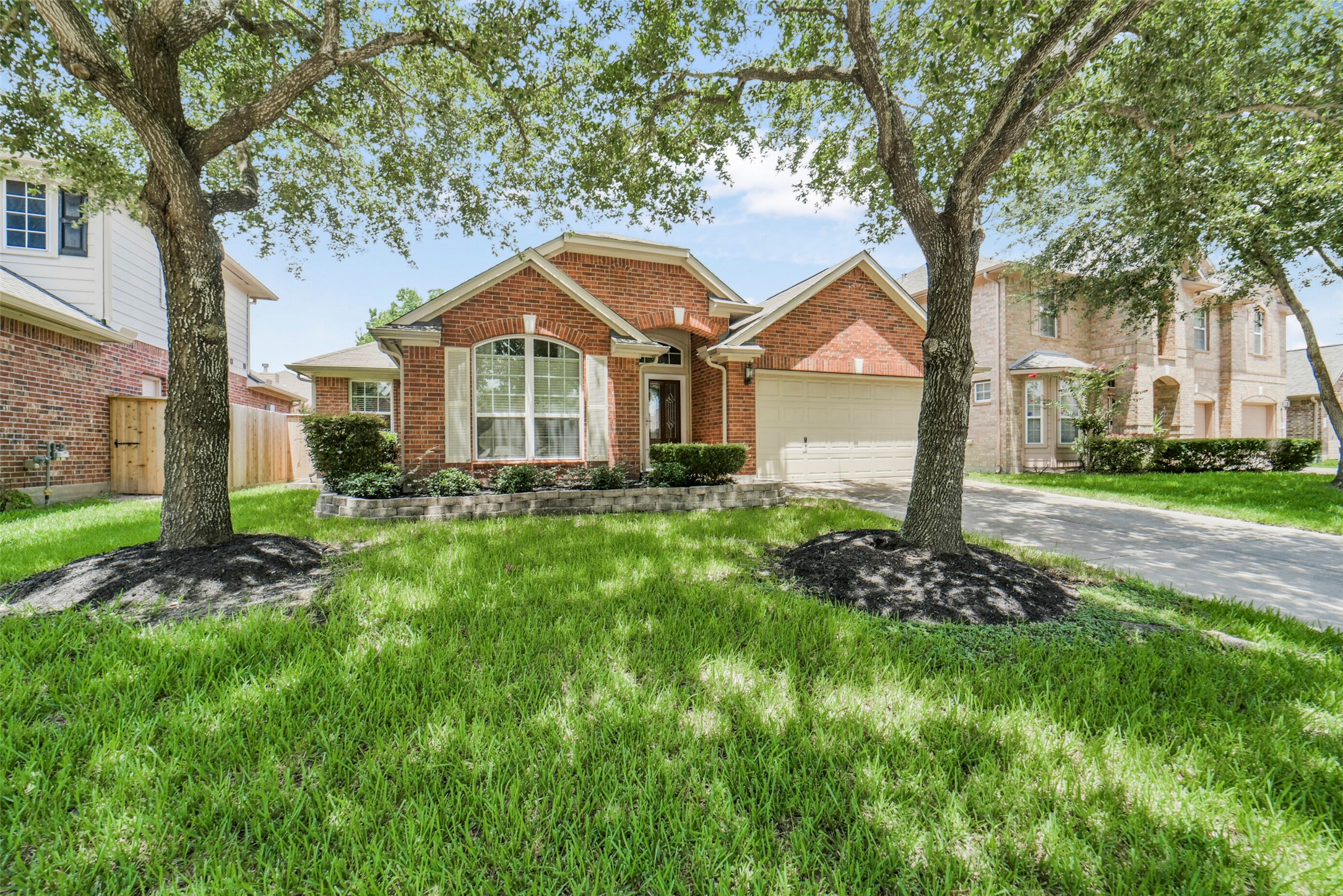 Charming brick home with a welcoming arched window and well-maintained landscaping, nestled between mature trees on a lush green lawn.