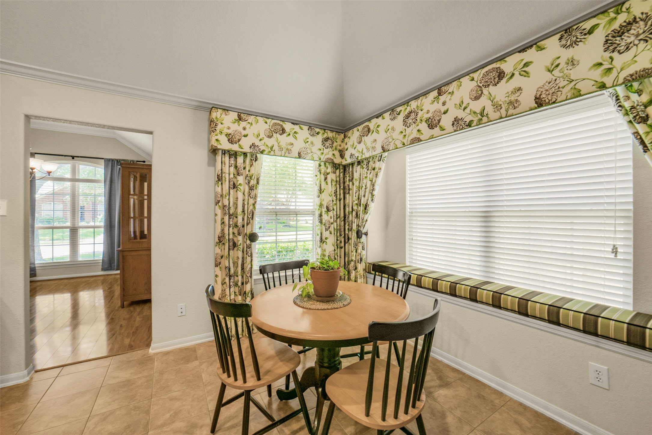 Charming breakfast nook with a cozy table set, surrounded by large windows adorned with floral curtains, offering a bright and inviting space.