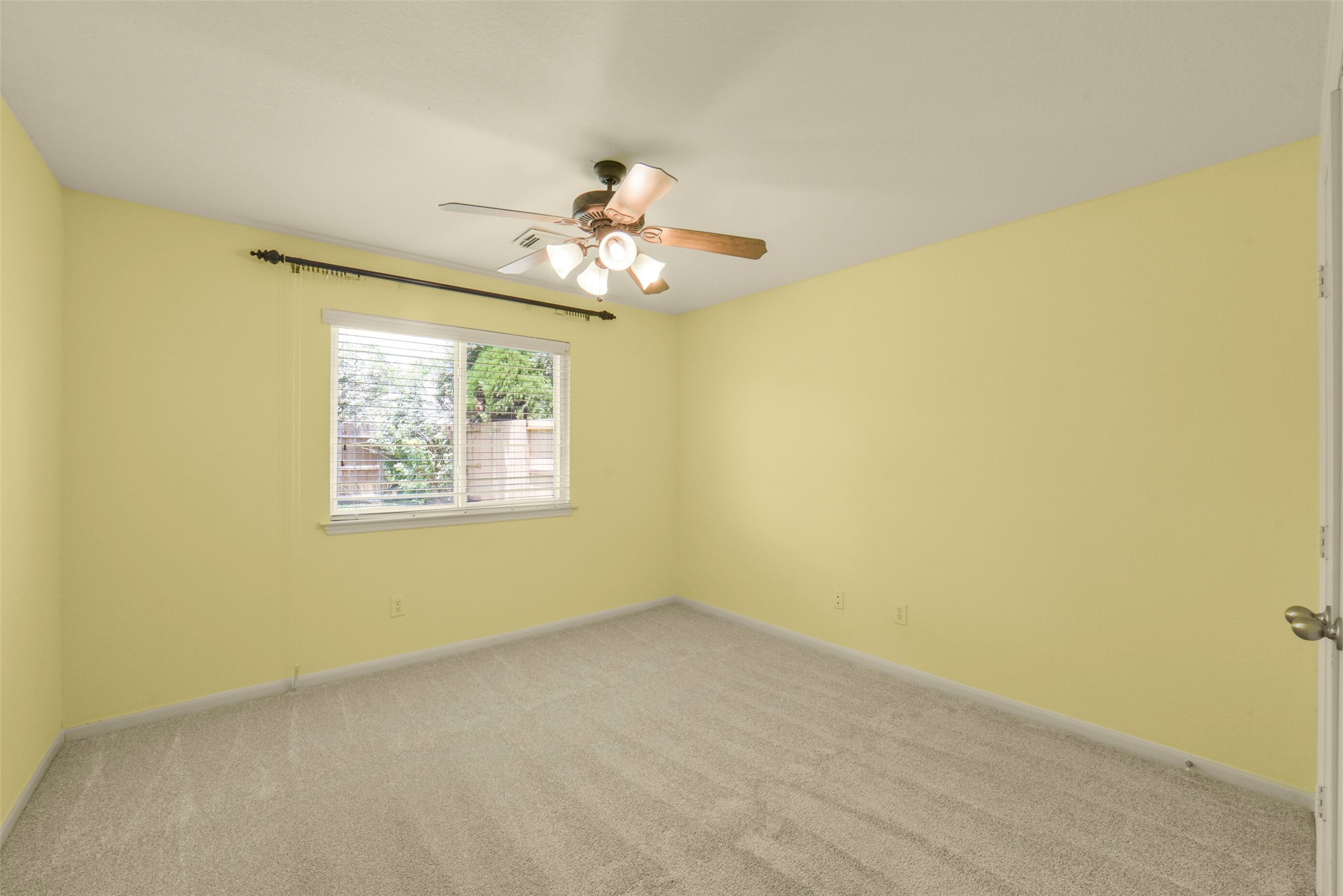Bright and cozy secondary bedroom with plush carpeting, and a ceiling fan, offering a peaceful view through a large window.