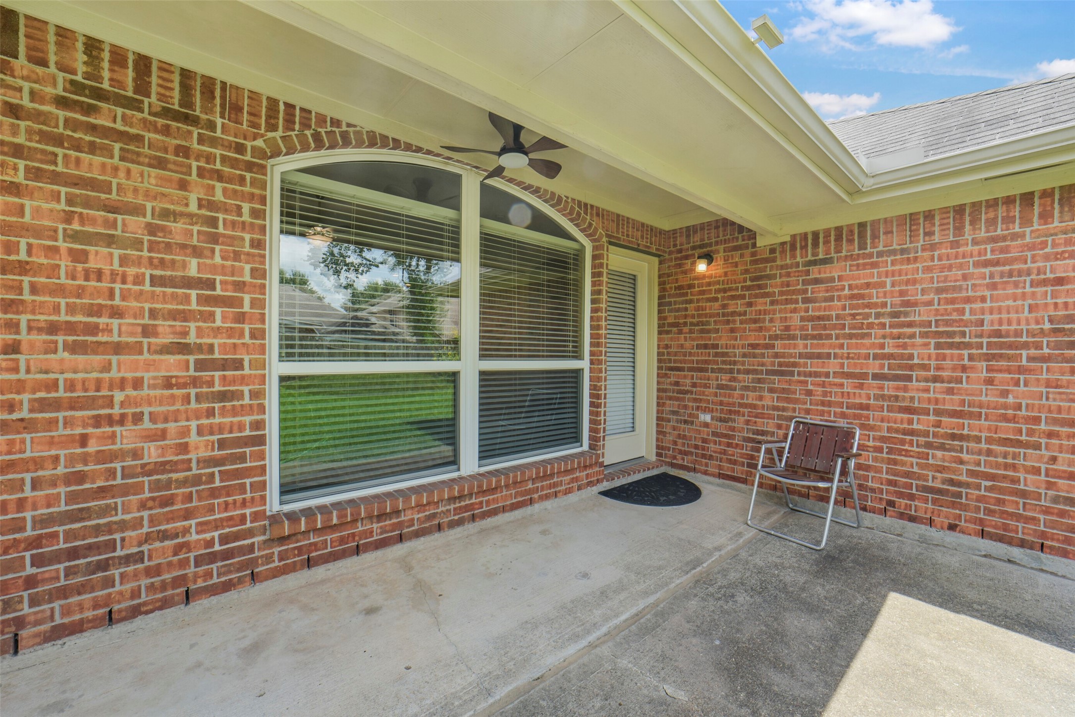 Charming covered patio with red brick exterior, featuring a large arched window and ceiling fan, perfect for relaxing outdoors.