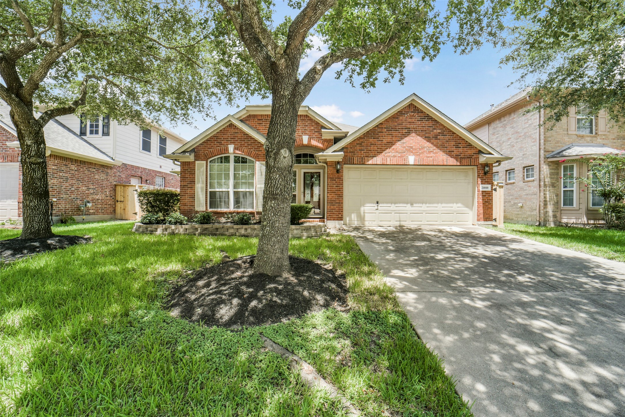 Charming brick home with a welcoming facade, mature trees, and a spacious driveway leading to a two-car garage.