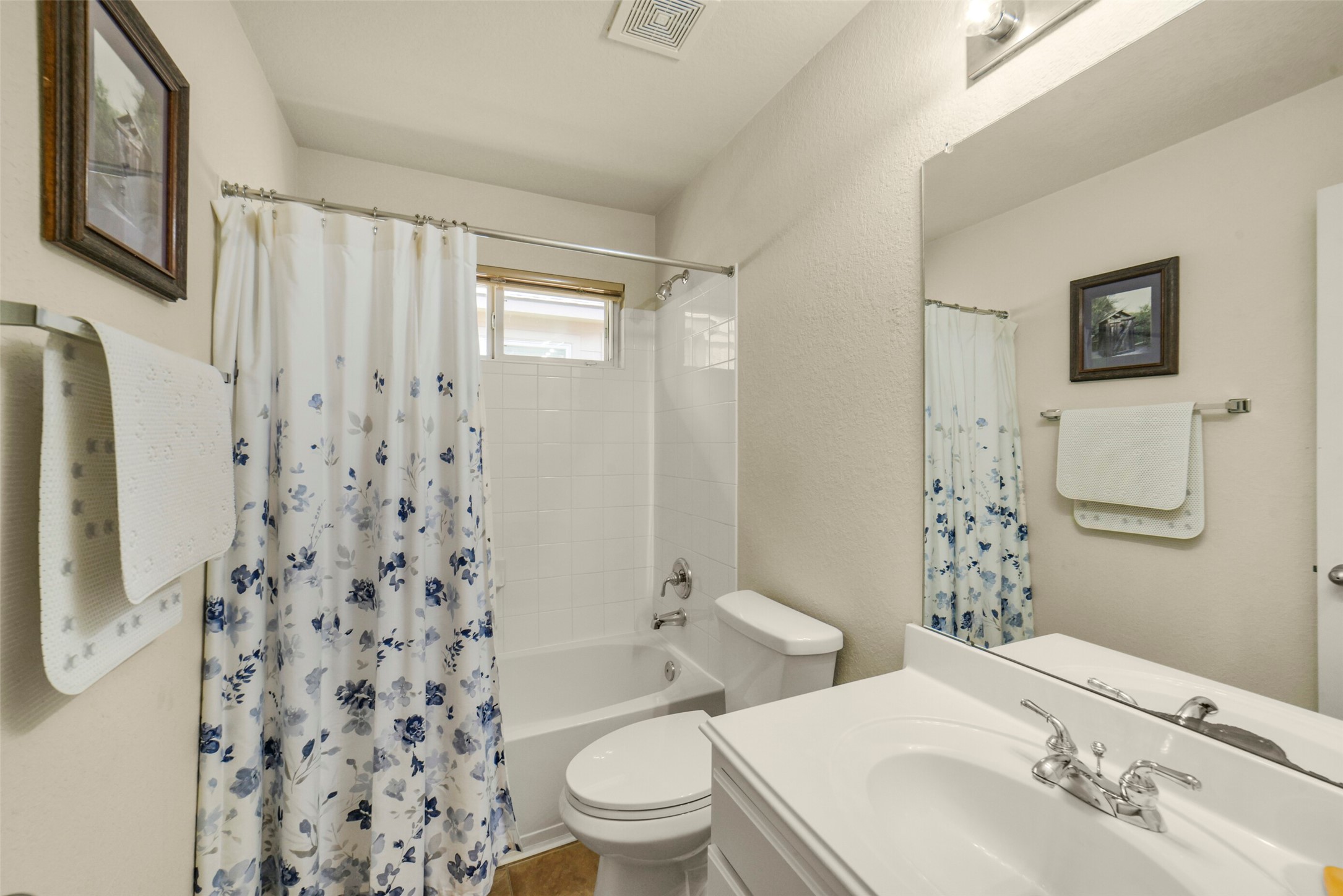 Charming secondary bathroom featuring a clean white vanity, classic shower-tub combo with floral curtain, and ample natural light.
