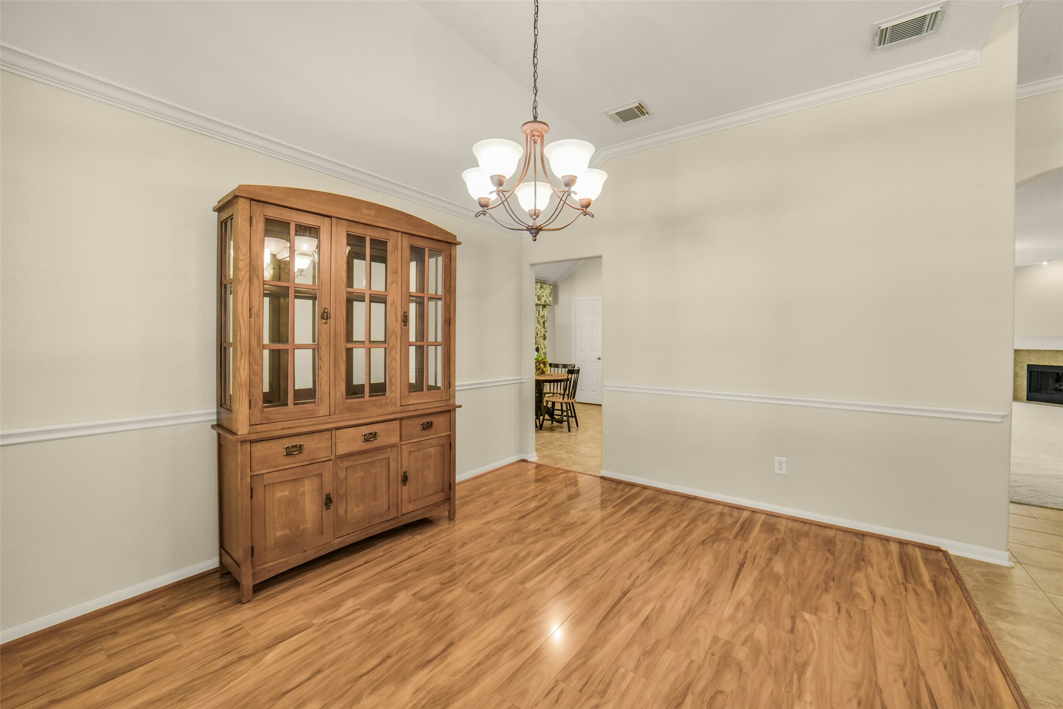 Elegant dining area with warm wood flooring, a classic wooden hutch, and a stylish chandelier, offering a cozy and inviting space for entertaining.