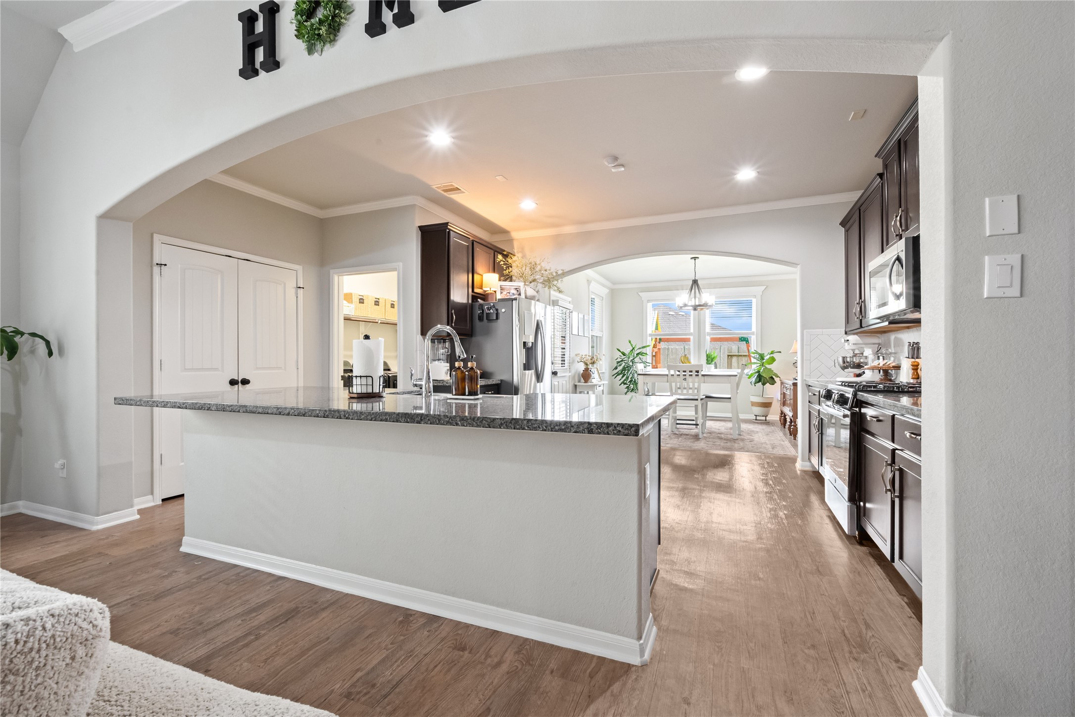 This photo showcases a modern kitchen with dark cabinetry, a large granite island, and stainless steel appliances. The open layout flows into a bright dining area, featuring wood flooring and elegant archways. Perfect for entertaining and family gatherings. This photo showcases a modern kitchen with dark cabinetry, a large granite island, and stainless steel appliances. The open layout flows into a bright dining area, featuring wood flooring and elegant archways. Perfect for entertaining and family gatherings.