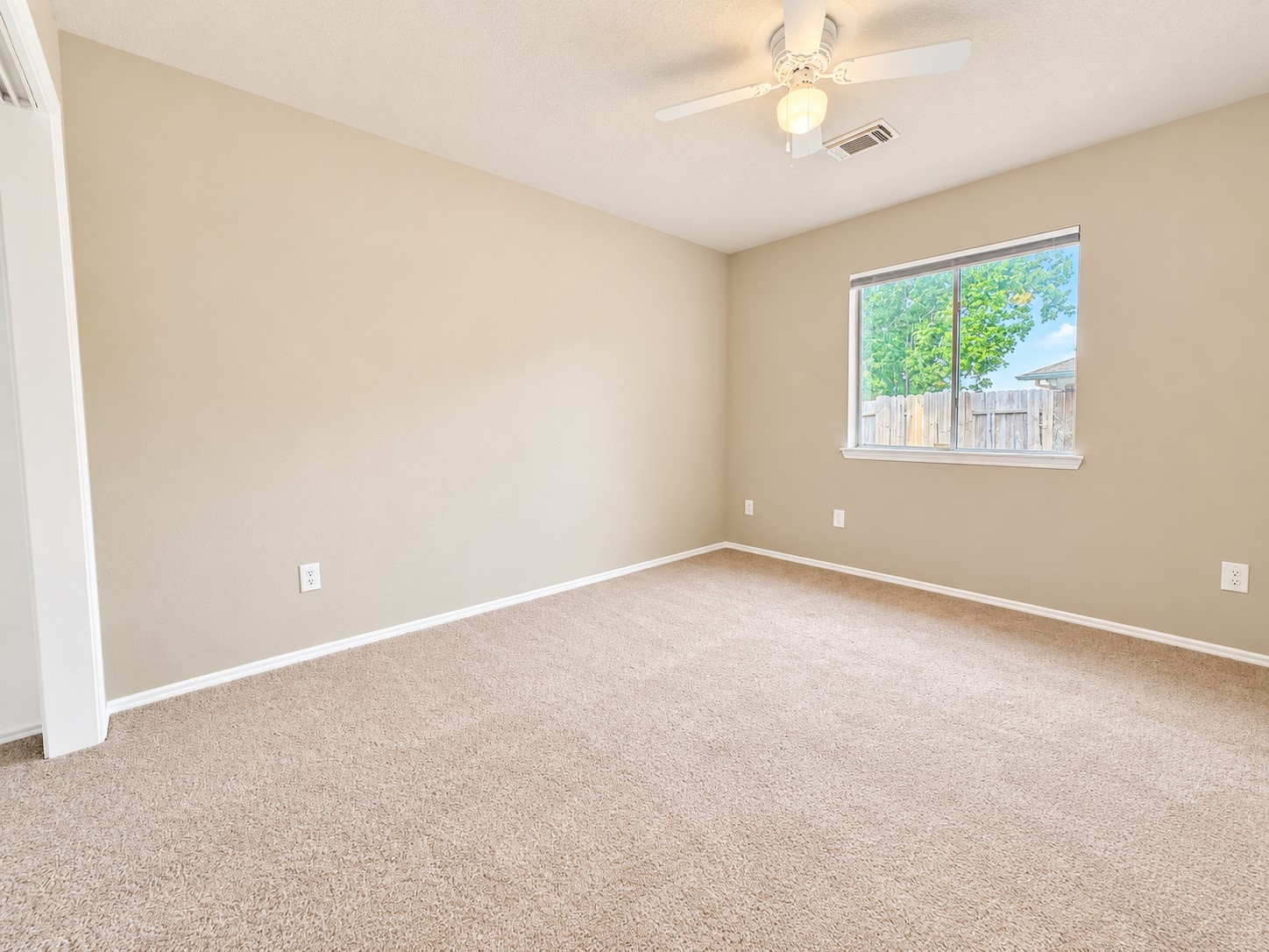 Third bedroom featuring neutral tones, soft carpeting, a ceiling fan, and a large window overlooking the backyard. New carpet.