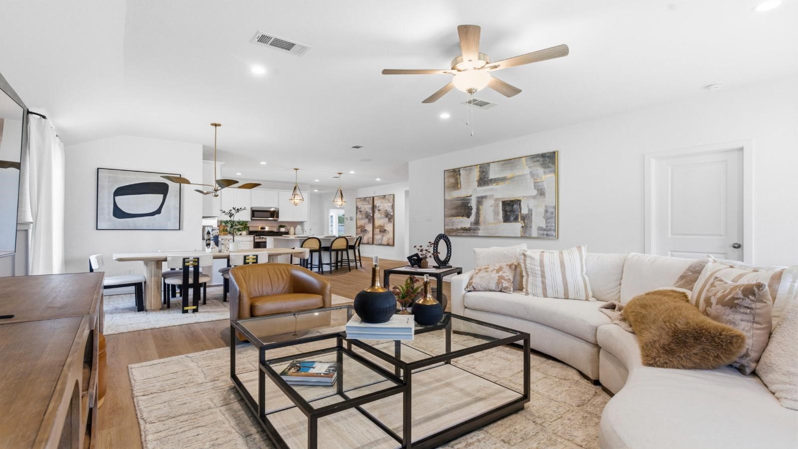 A cozy living room featuring large windows for natural lighting, vinyl wood flooring and a view to the kitchen and dining area.