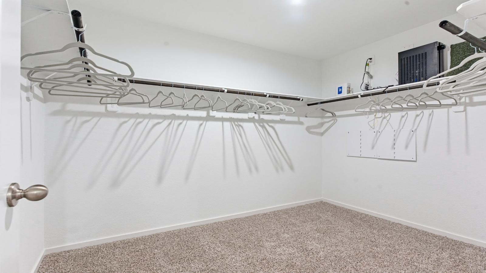 A spacious walk-in closet off the primary bathroom with multiple hanging rods, and shelves for maximum storage capabilities.