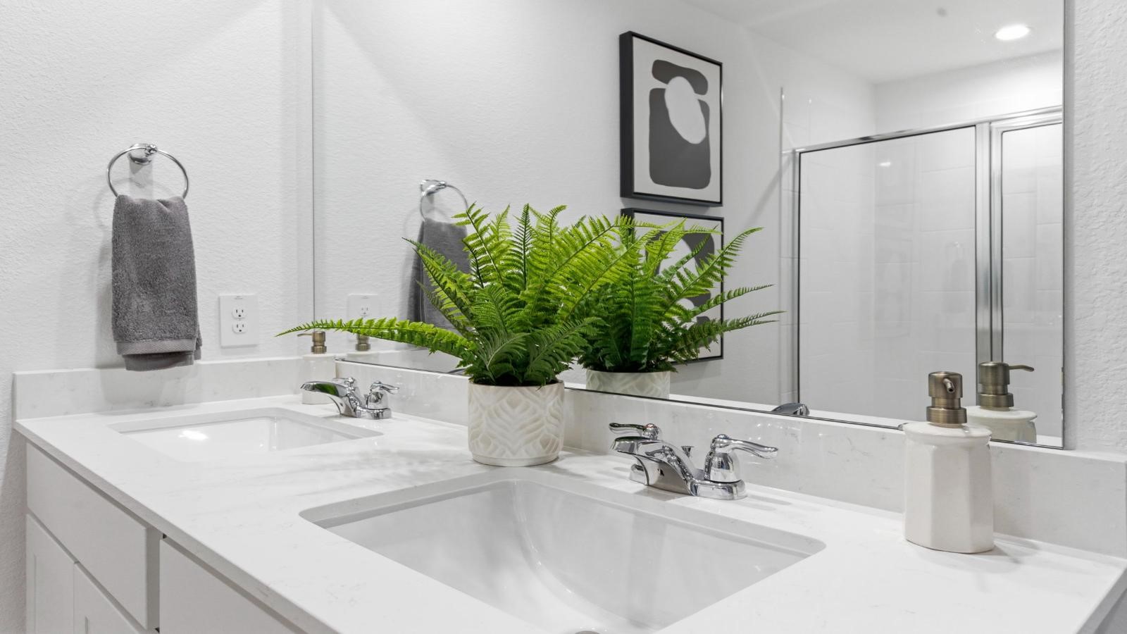 Modern primary bathroom with double vanities, quartz countertops, and a glass-enclosed shower with a walk-in closet.
