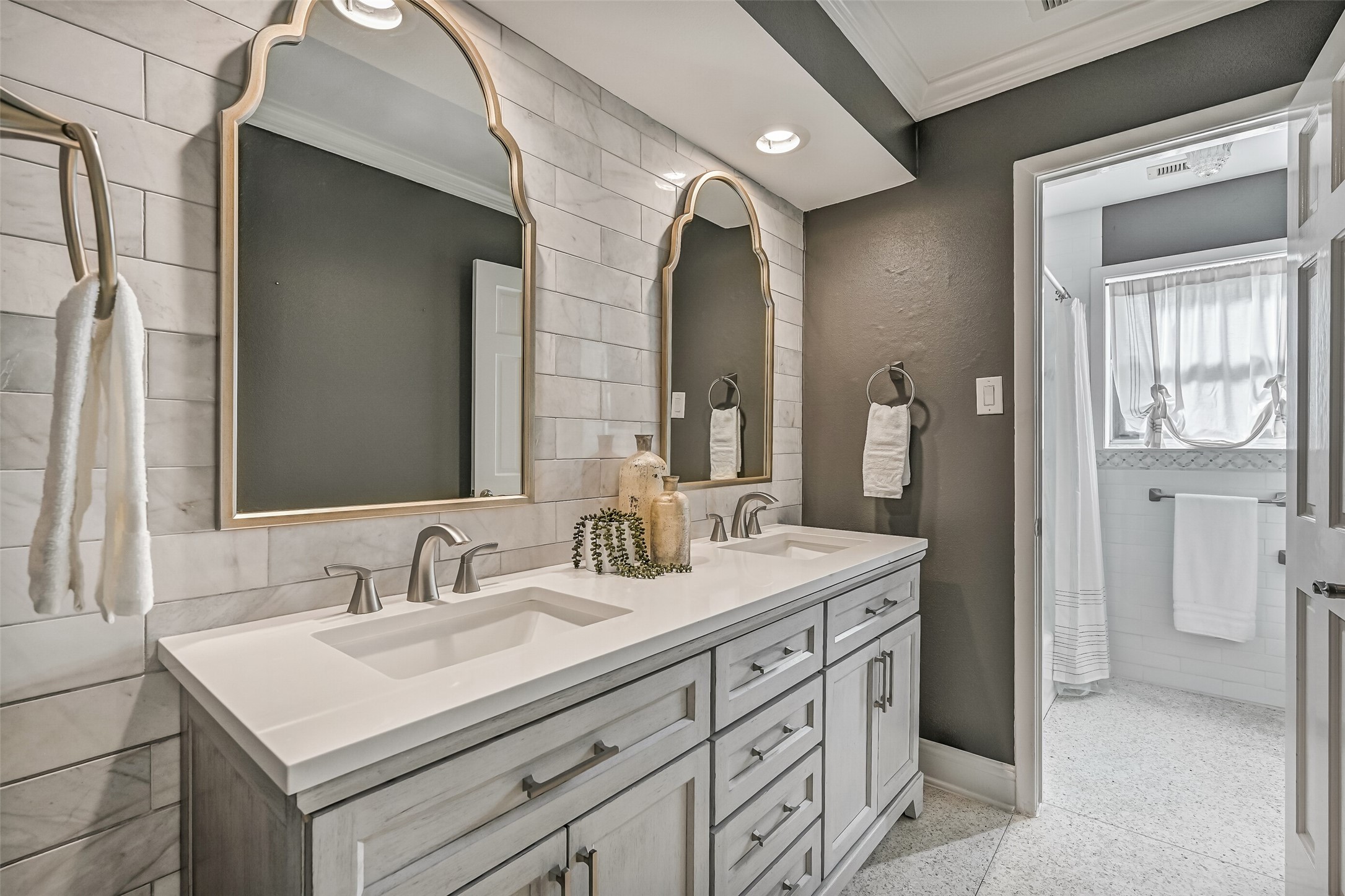 Guest Bathroom  First Residence:
The stylishly updated guest bath showcases a furniture-style double vanity with quartz countertops, dual undermount sinks, and custom framed mirrors set against a tiled accent wall. The bath includes a tub/shower combination with a classic white subway tile surround & decorative mosaic inlay.