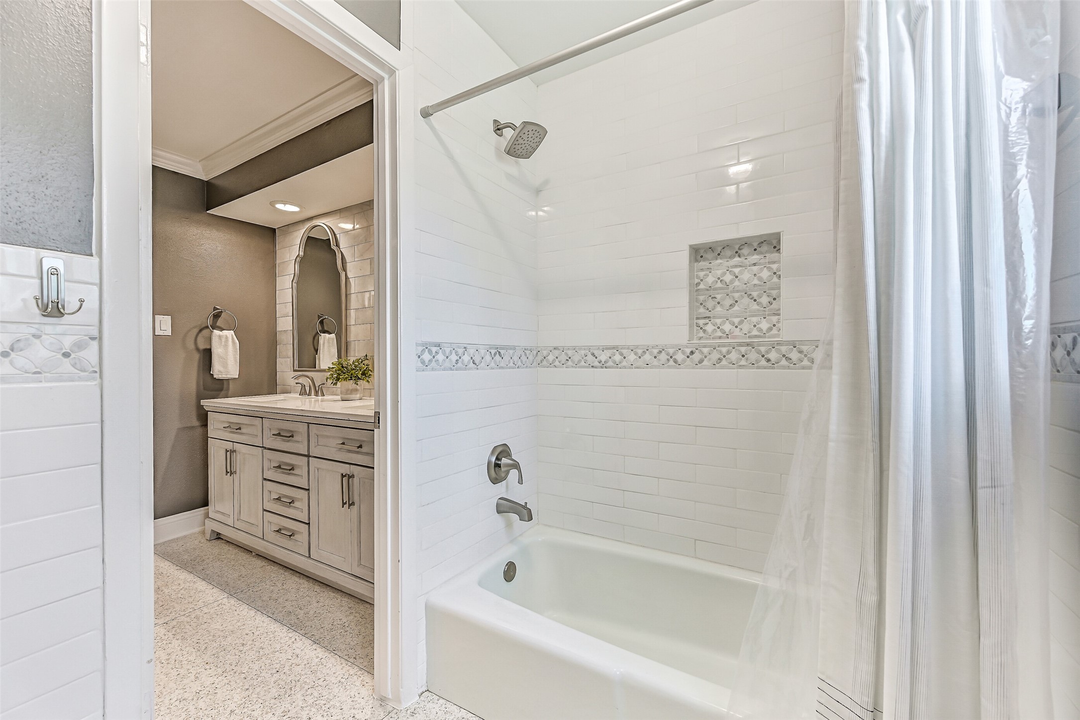 Guest Bathroom  First Residence:
The stylishly updated guest bath showcases a furniture-style double vanity with quartz countertops, dual undermount sinks, and custom framed mirrors set against a tiled accent wall. The bath includes a tub/shower combination with a classic white subway tile surround & decorative mosaic inlay.