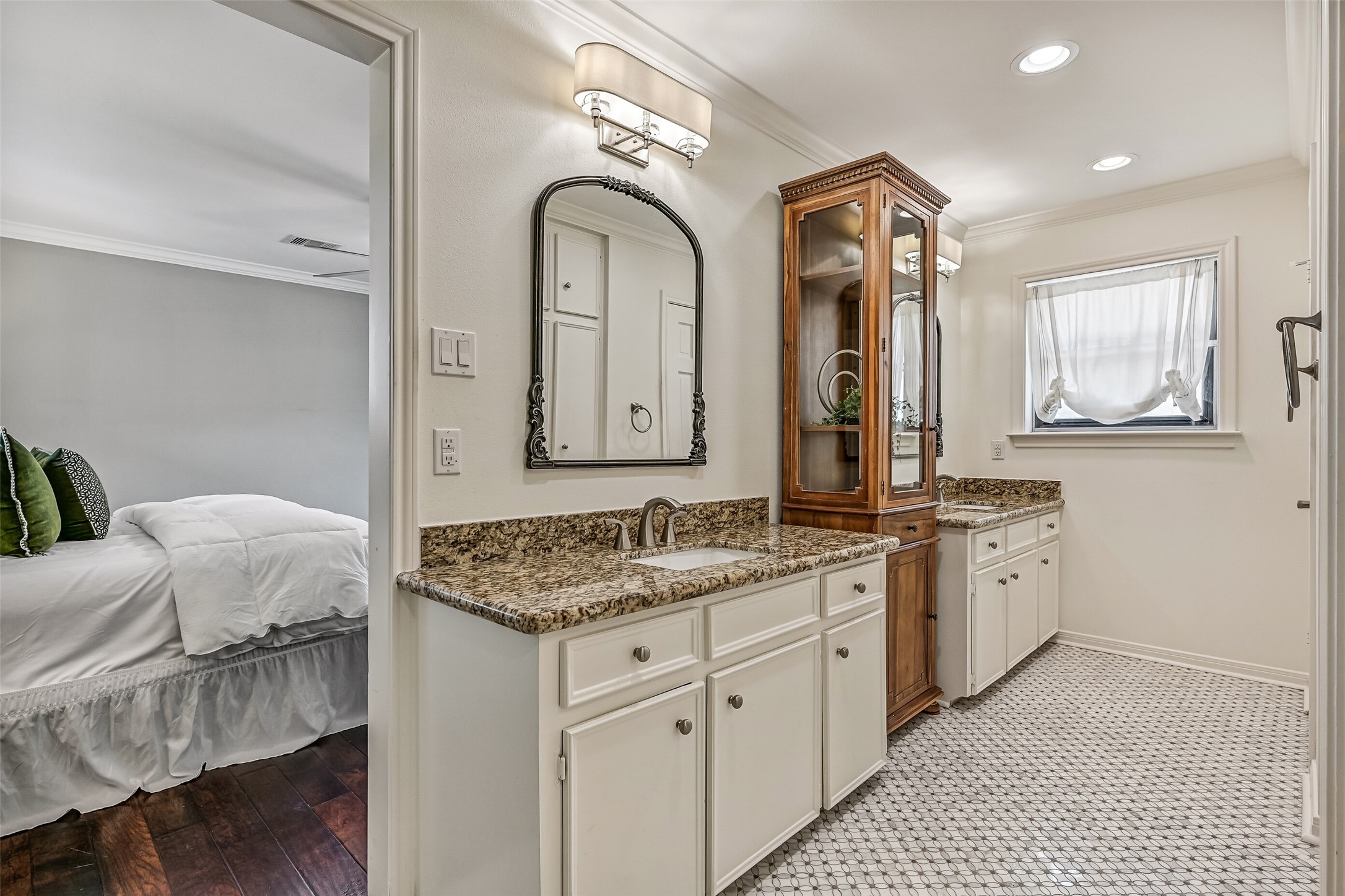 Master Bathroom  First Residence:
The master bath boasts dual vanities with granite countertops, abundant cabinetry, separated by a tower style storage cabinet. Recessed lighting, classic tile flooring, and a window providing natural light create a bright, functional, and roomy layout.