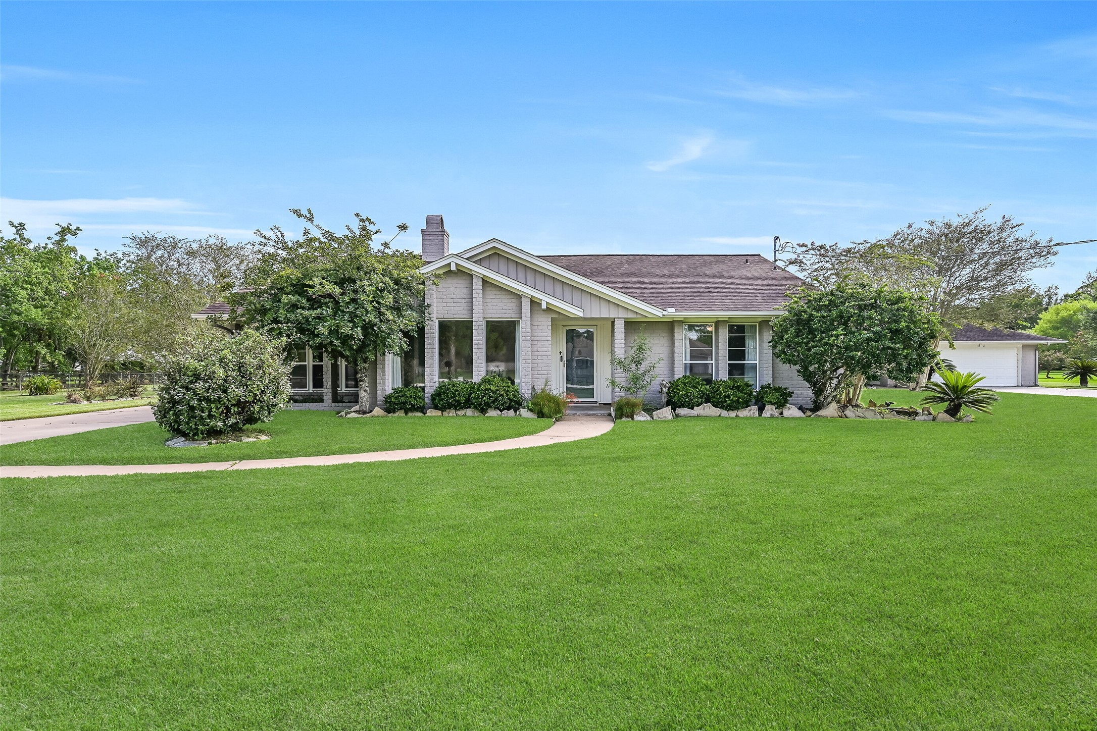 Front Elevation  First Residence:
The first residence boasts a classic painted brick exterior with a covered entry, manicured landscaping, and a long private driveway, all positioned on a spacious 1.3-acre lot.