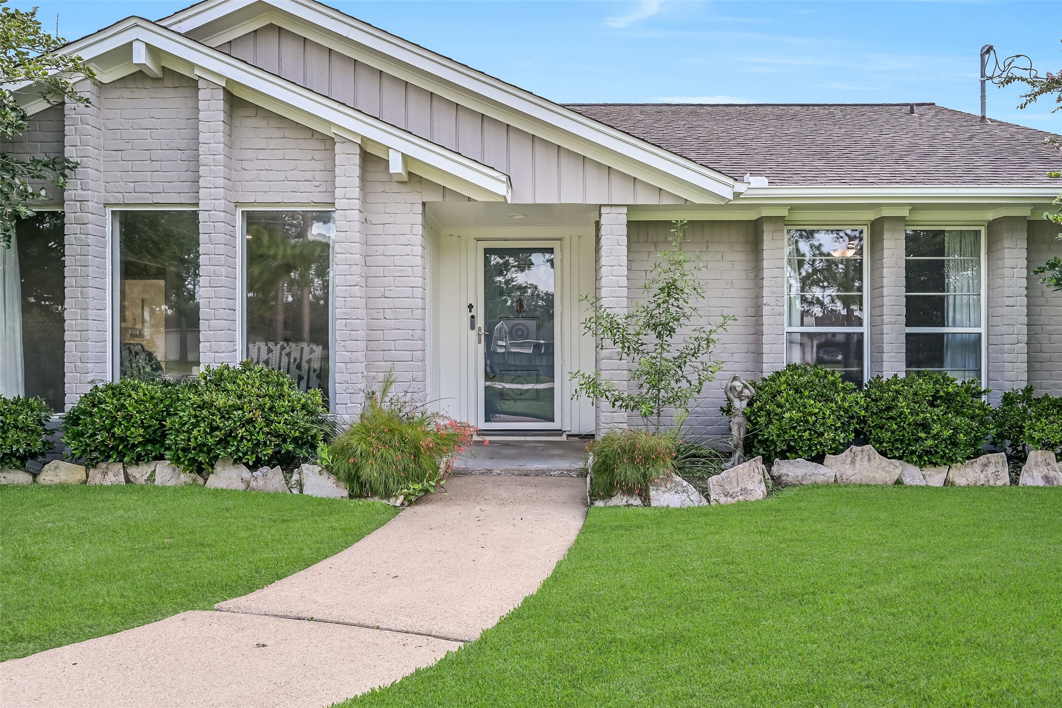Front Porch  First Residence:
A concrete path winds from the driveway of the first home to this covered front porch with brick columns, charming gabled rooflines, and a recessed entry, complemented by manicured landscaping.