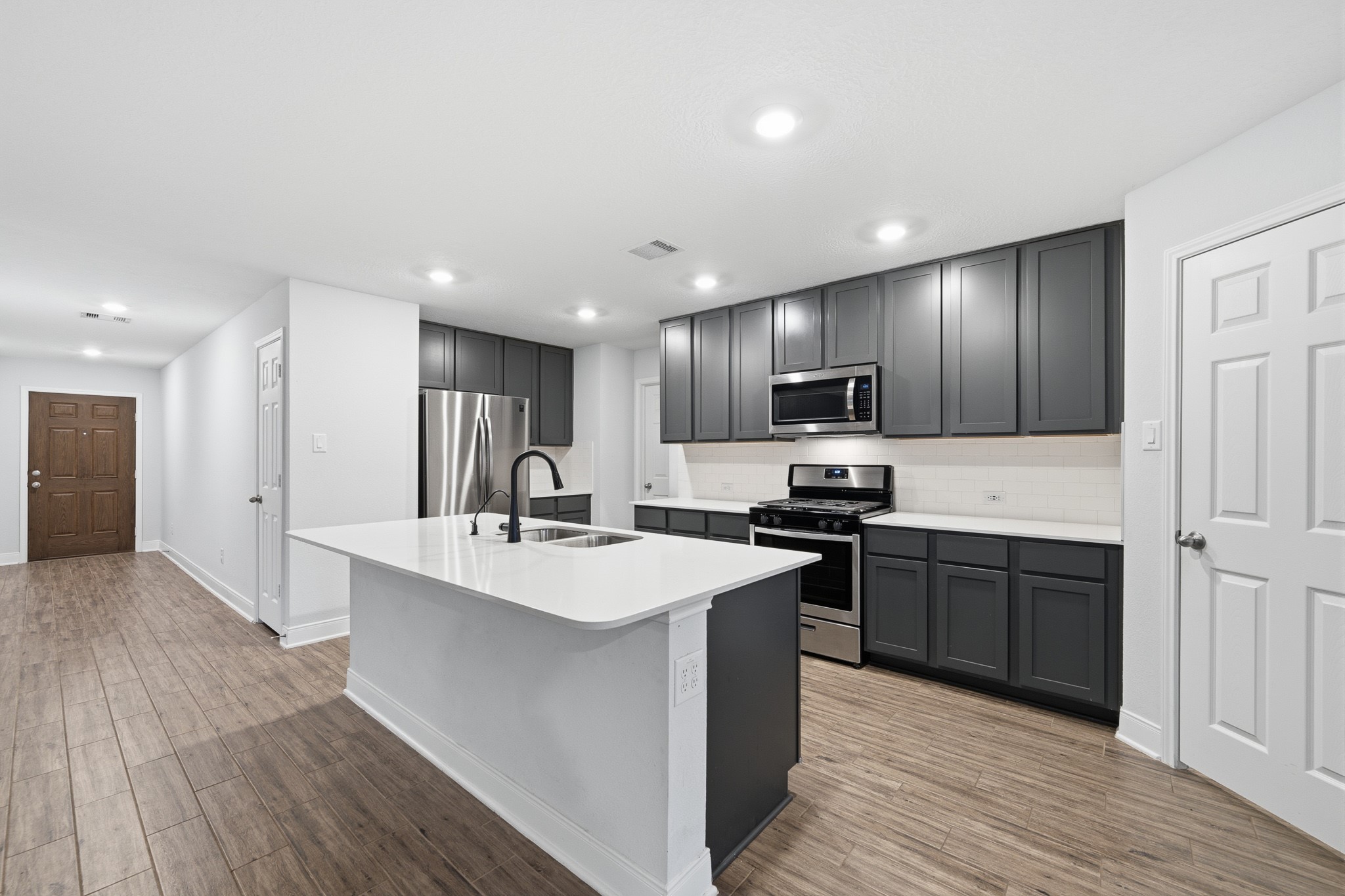 Modern kitchen with sleek gray cabinetry, stainless steel appliances, and a spacious island, complemented by sleek flooring and bright recessed lighting.