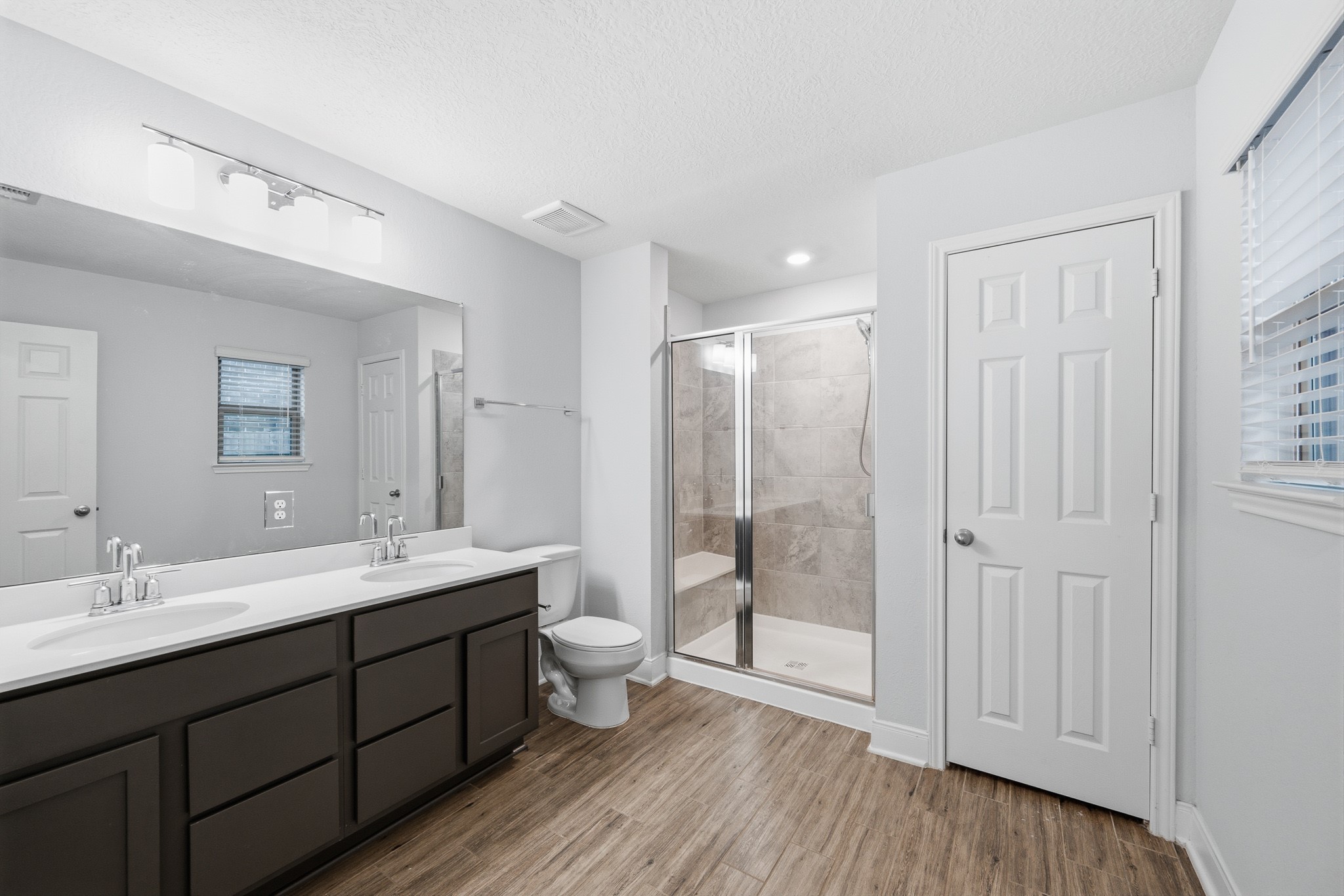Spacious bathroom featuring a double vanity with modern fixtures, a glass-enclosed shower, and sleek flooring for a contemporary feel.