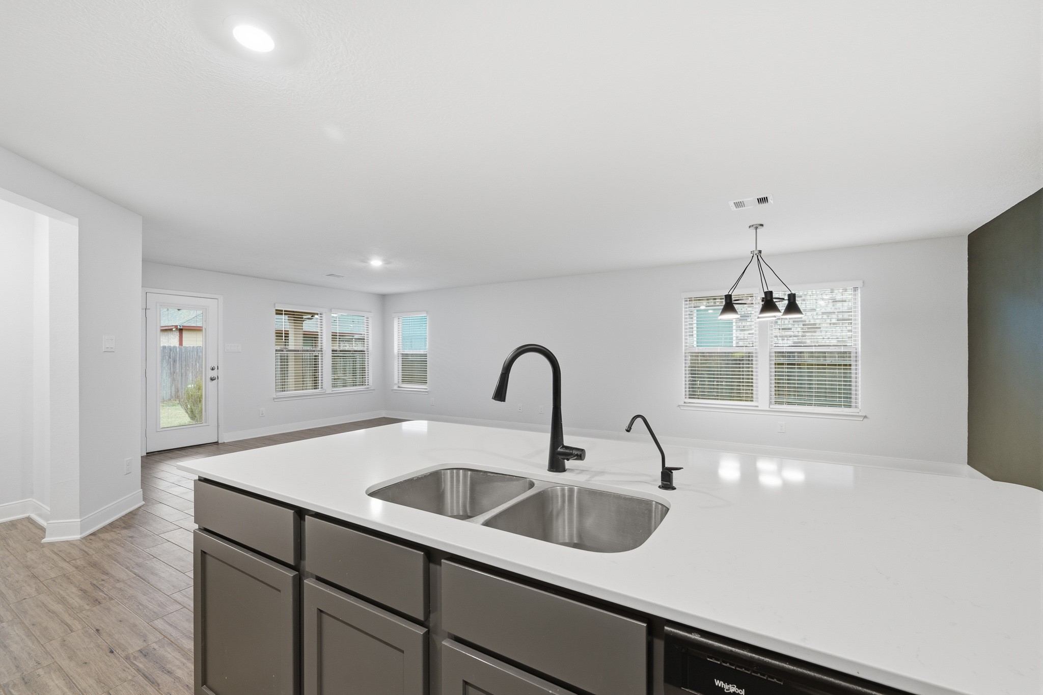Spacious open-plan kitchen and living area featuring a sleek island with a modern sink, stylish light fixtures, and abundant natural light from large windows and a patio door.