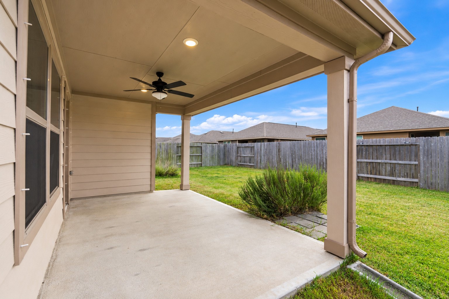 Charming covered patio with a ceiling fan overlooks a spacious fenced backyard, perfect for outdoor relaxation and family fun.