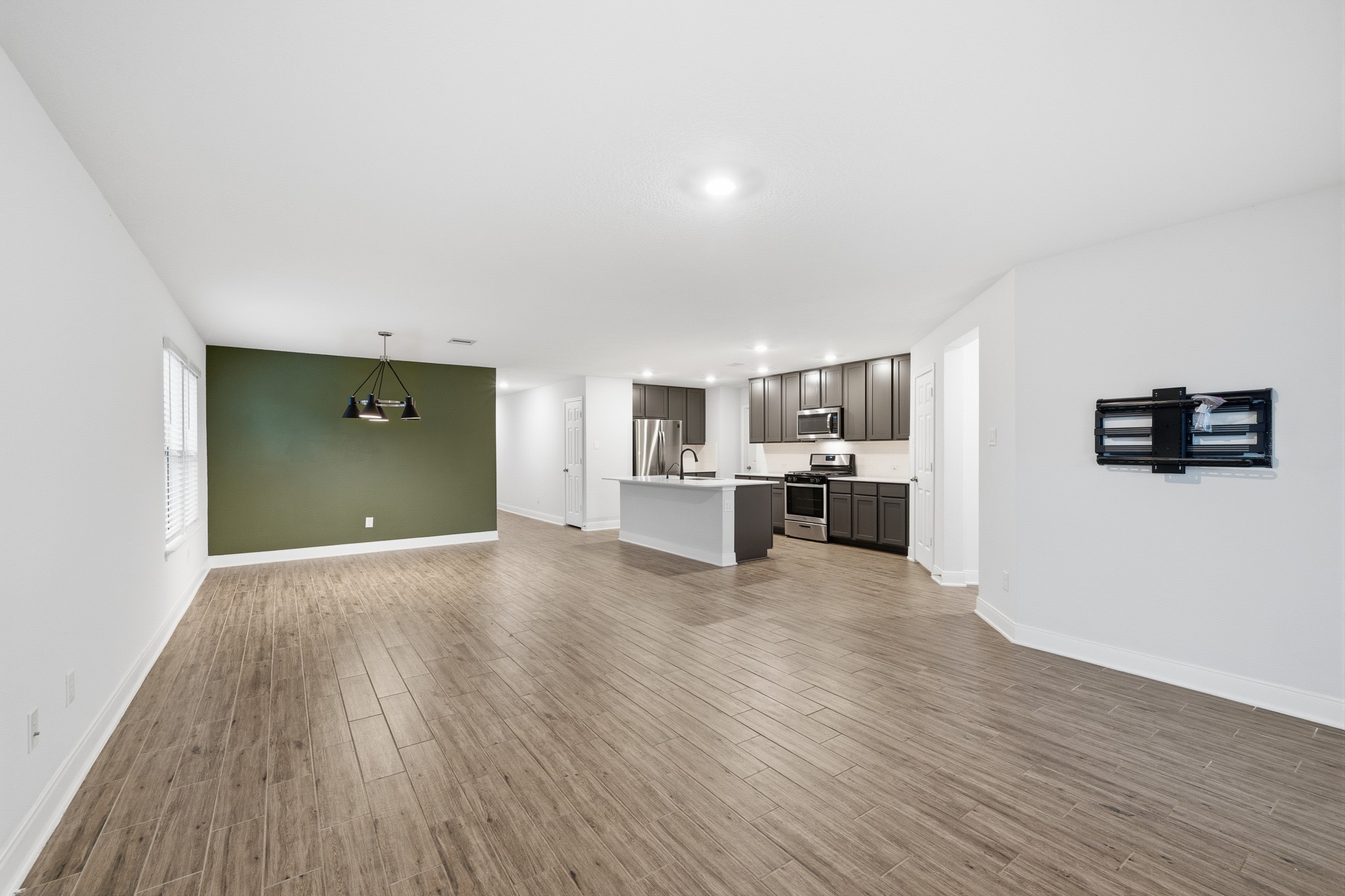 Spacious open-concept living area featuring sleek flooring, a modern kitchen with stainless steel appliances, and a stylish accent wall perfect for dining.