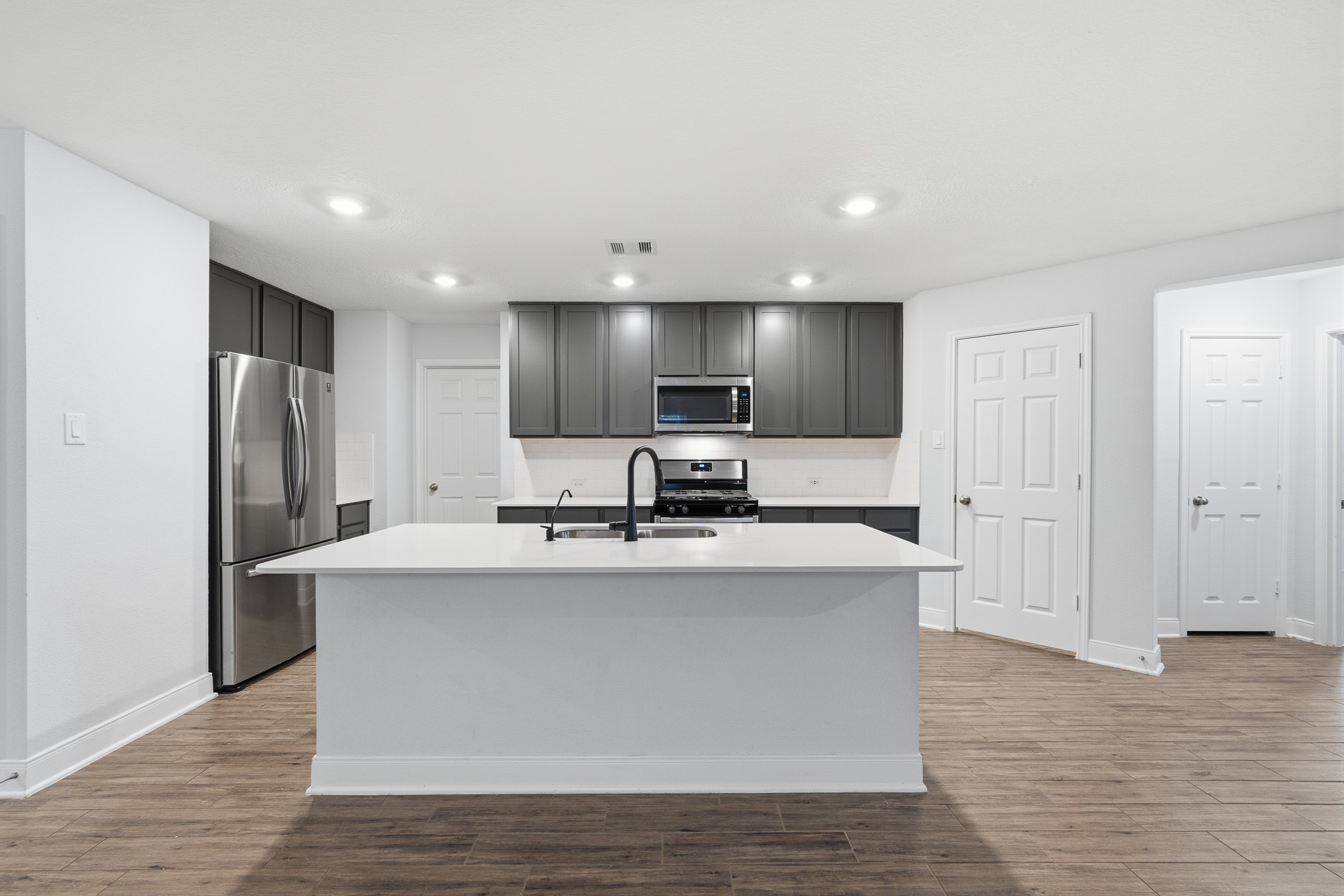 Modern kitchen featuring sleek dark cabinetry, stainless steel appliances, and a spacious island with a stylish sink.