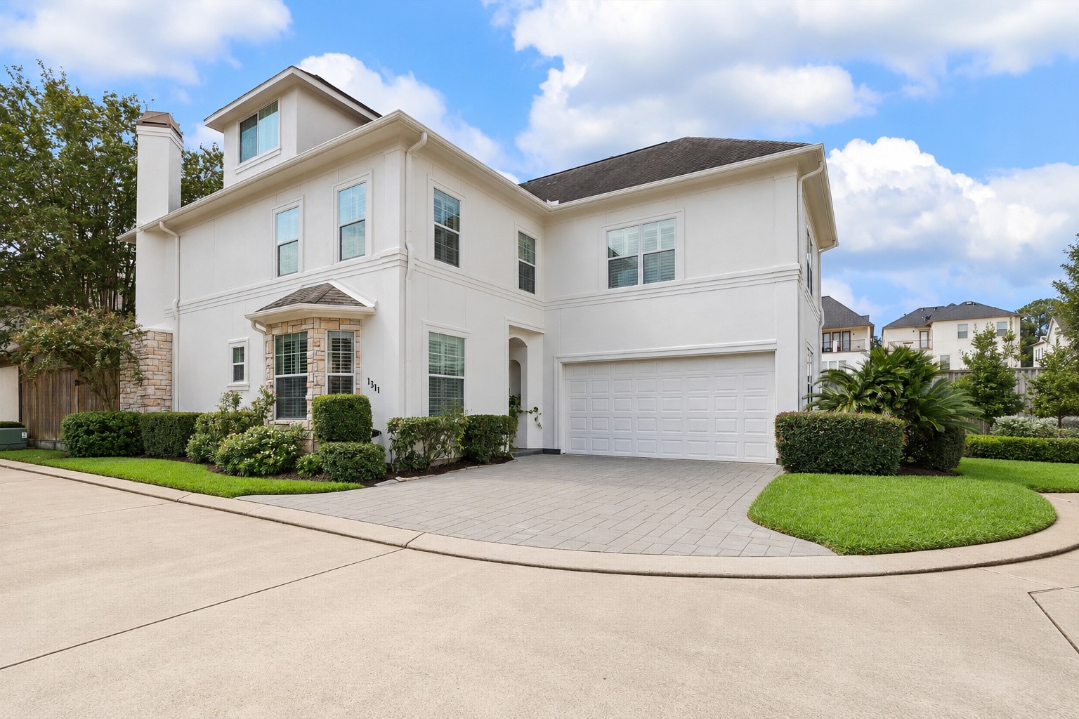 Another view of this lovely home highlighting the covered entry w/ recessed lighting, attached 2-car garage w/ built-in storage & EV charging outlet, and double-wide driveway. Wonderful lock & leave lifestyle w/ HOA dues covering water, twice-weekly trash collection, weekly basic lawn maintenance & common area maintenance. Conveniently located near major freeways, Downtown, Galleria & Energy Corridor! (Photo virtually enhanced to show power-washed driveway).