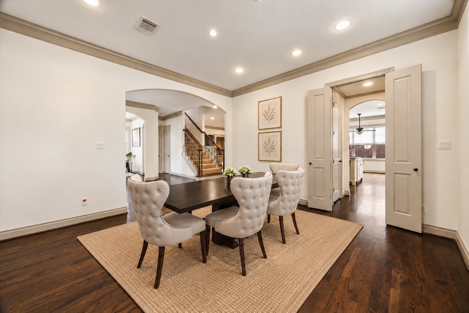 Another view of the spacious formal dining room showcasing beautiful hardwood floors, crown molding & abundant wall space for artwork or additional furnishings. French doors to the right lead directly to the butler's pantry & kitchen, providing convenient access for serving & entertaining. Wonderful layout for both intimate dinners & larger gatherings! Virtually staged.
