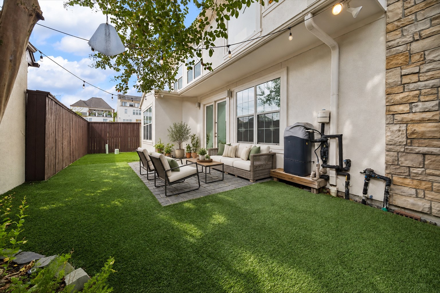 Another perspective of the inviting backyard showcasing the combination of paved patio & turfed green space. String lights, outdoor speakers & floodlights create a wonderful setting for outdoor gatherings, morning coffee or relaxing at the end of the day. Half of the turf was replaced in 2026! (Photo virtually enhanced/furnishings virtually staged).