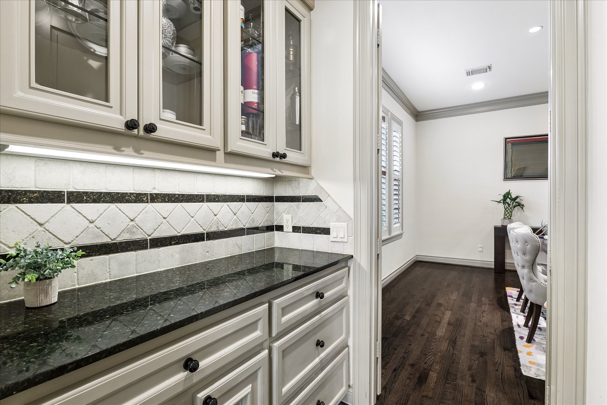 Dedicated dry bar/butler's pantry thoughtfully positioned between kitchen & formal dining room offers additional storage & serving space. Granite countertops, cabinetry & drawers below, and glass-front display cabinets above provide the perfect place for serving pieces & glassware. A wonderful feature for entertaining! Door to right leads to walk-in pantry.