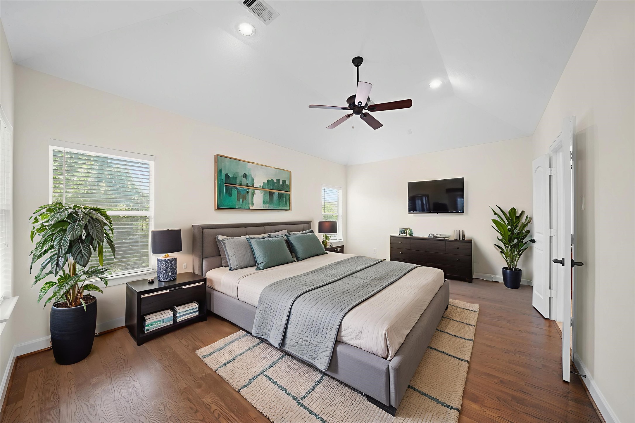 Virtually Staged: The primary bedroom includes hardwood floors, a high vaulted ceiling, recessed lighting, and windows with privacy blinds.