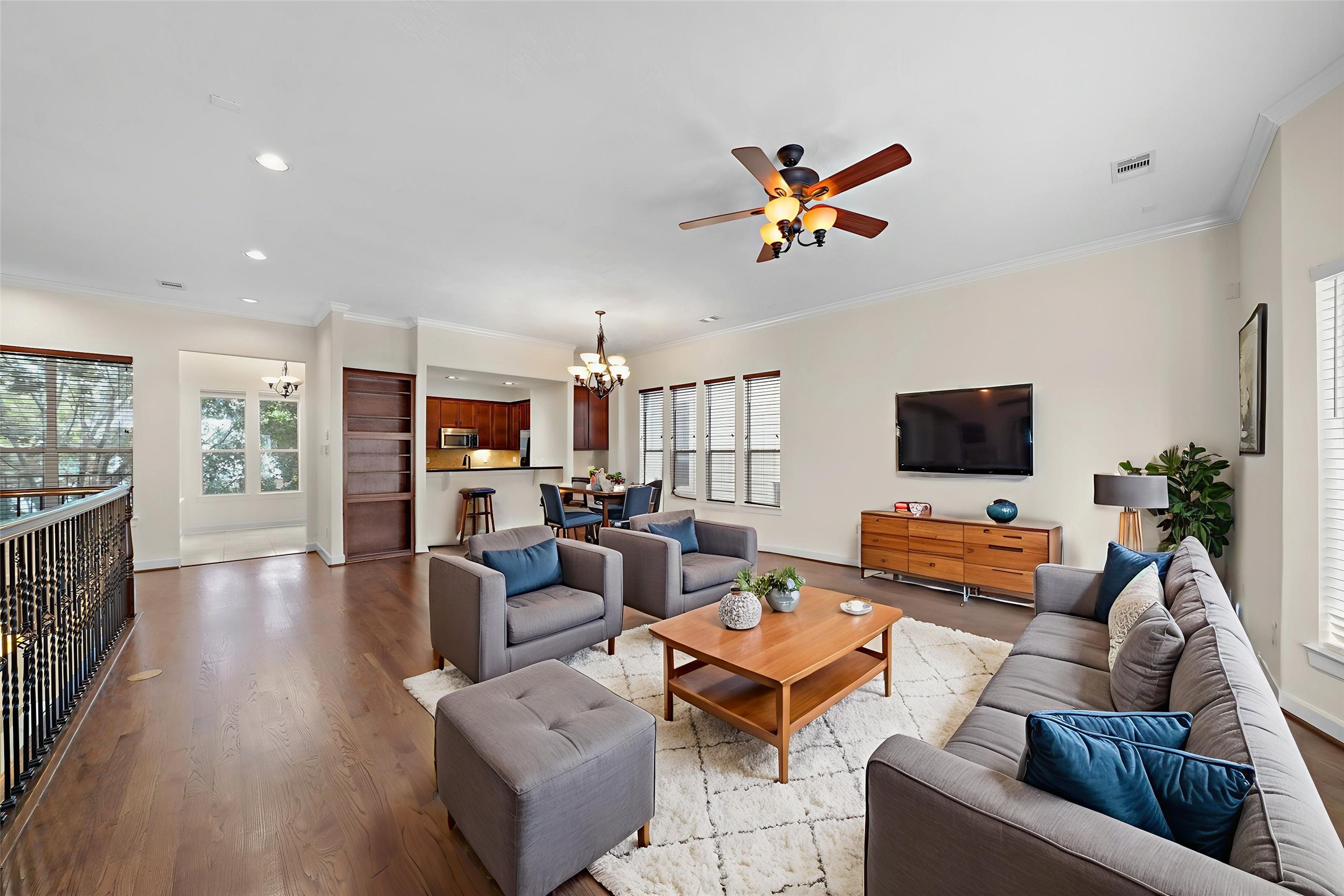 Virtually Staged: The open floor plan smoothly connects the dining and living areas. It includes crown molding details, a ceiling fan, hardwood floors, windows with privacy blinds, and recessed lighting.