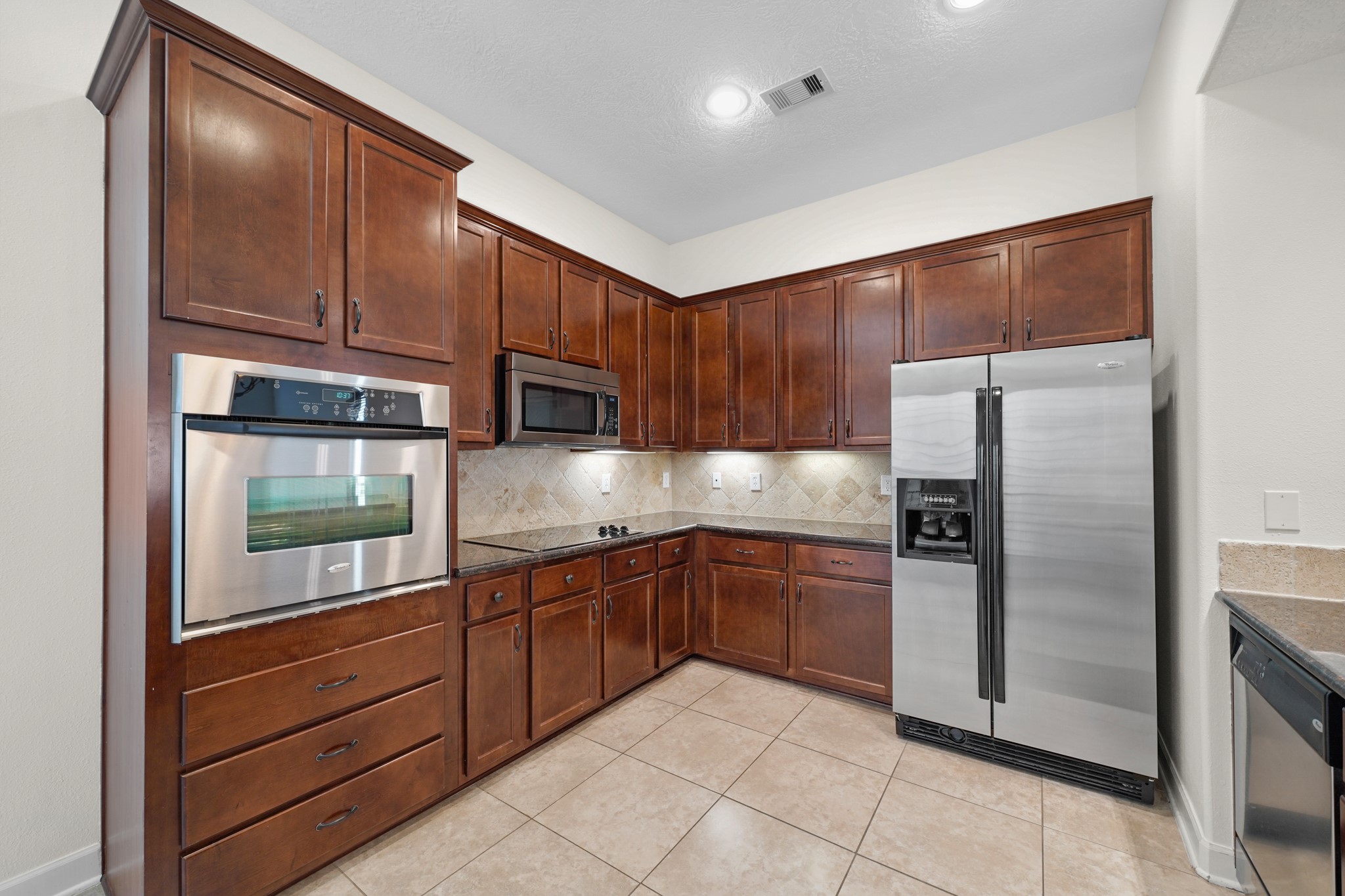 The kitchen has tile floors, recessed lighting, stainless steel appliances, tons of cabinetry for storage, and under cabinet lighting.