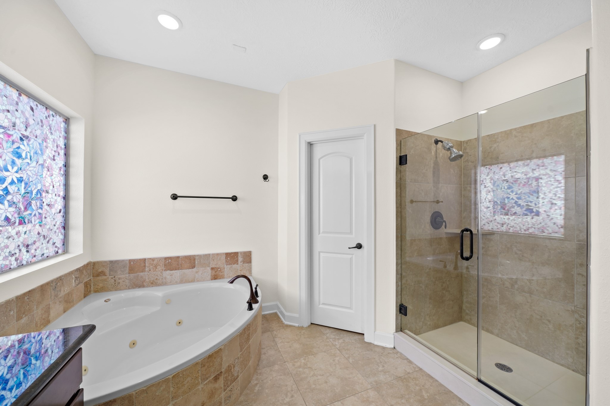 The master bath is highlighted by a jetted tub, private frozen glass window, recessed lighting, and a walk-in glass enclosed shower.